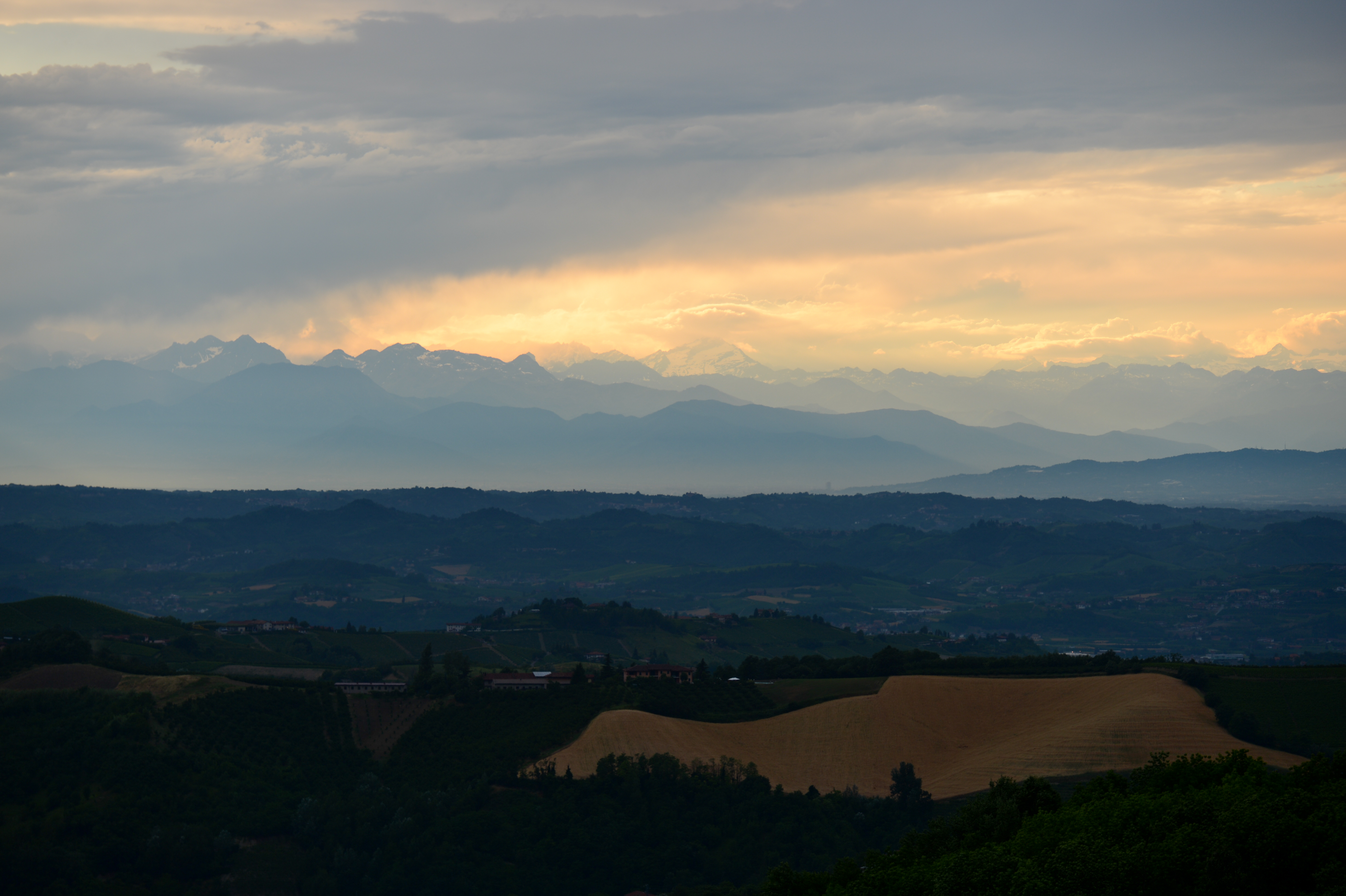 A scenic view of rolling hills and distant mountains under a cloudy sky with warm light at the horizon.
