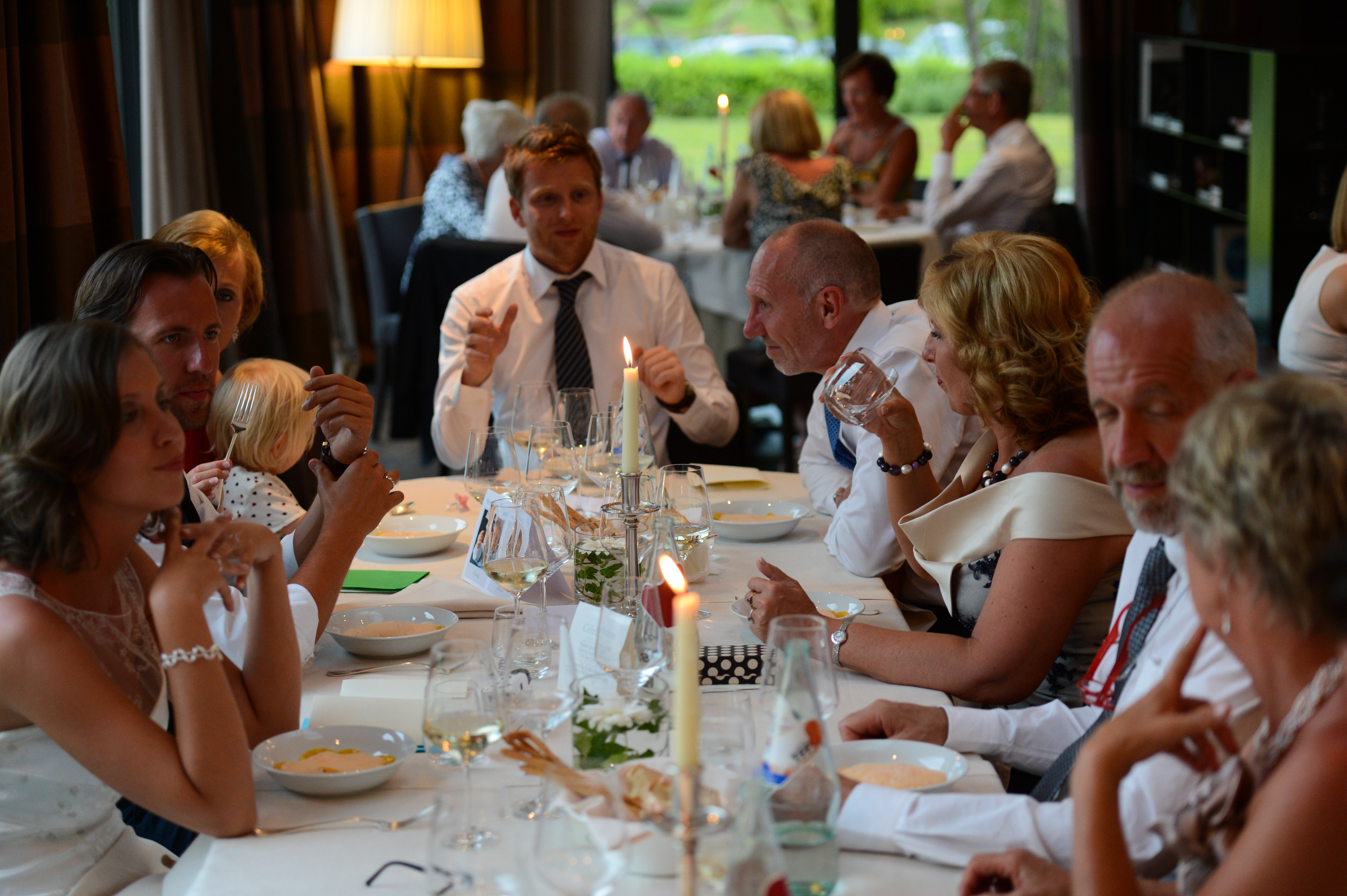 Wedding guests sit at a decorated table, eating, drinking, and talking during a reception dinner.