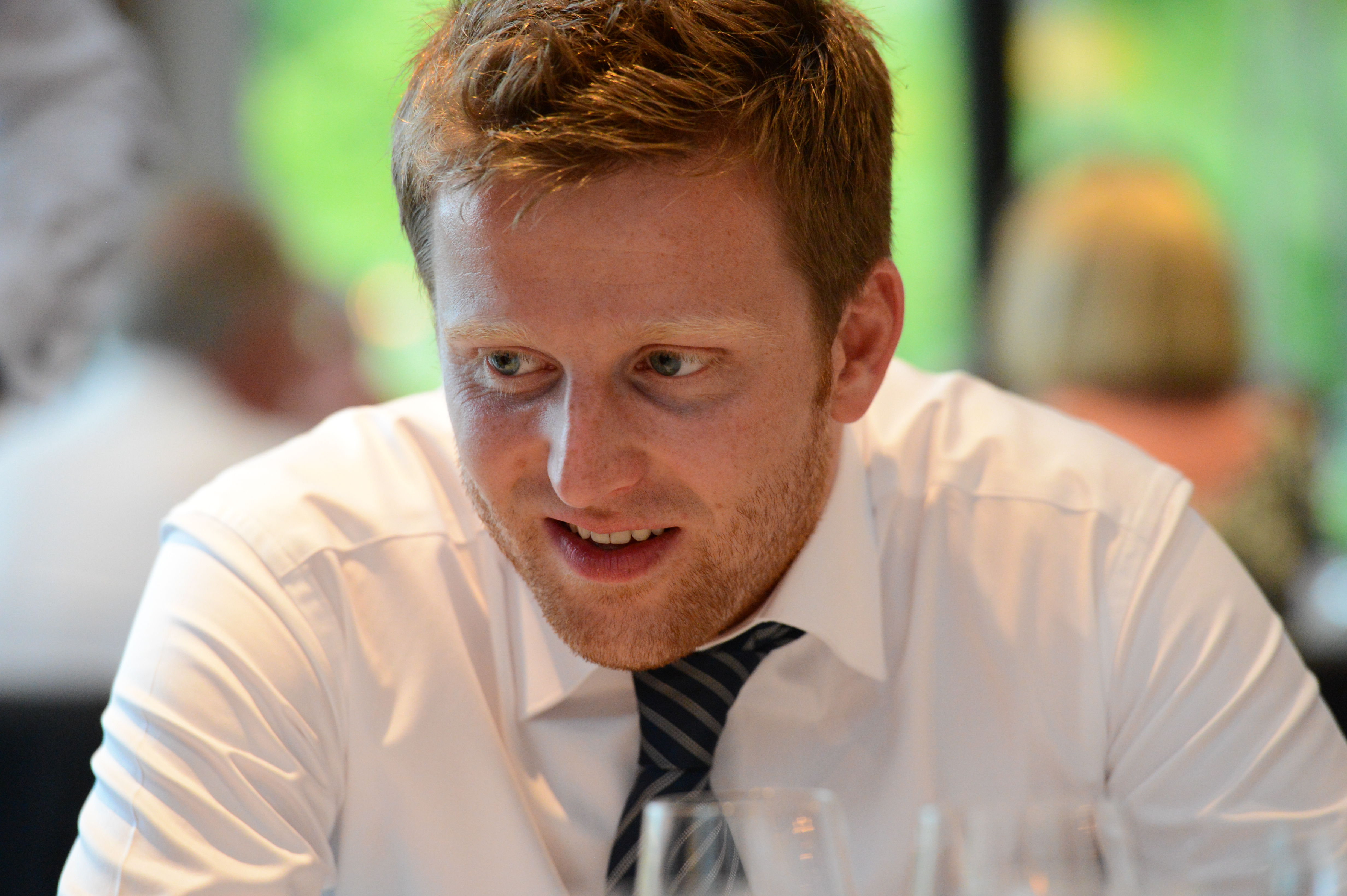 A man in a white shirt and striped tie smiles while seated at a wedding reception.