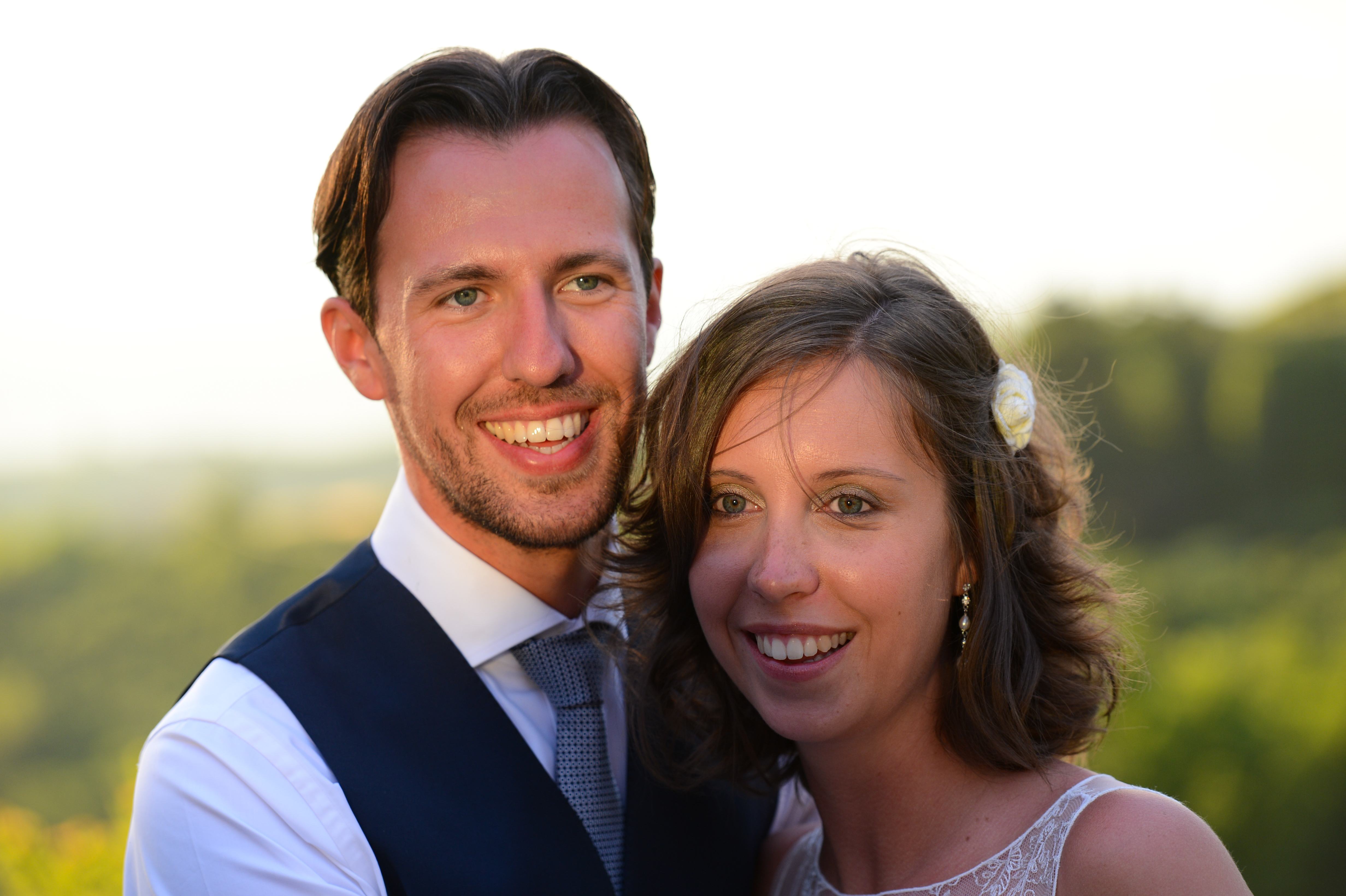 A smiling bride and groom pose together outdoors on their wedding day.