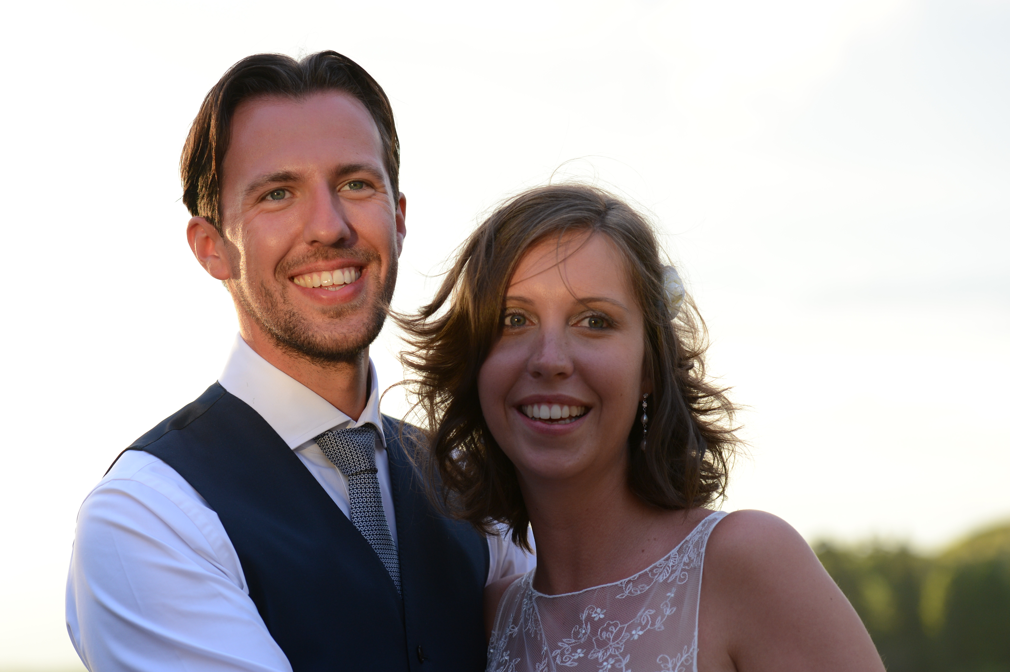 A smiling bride and groom pose together on their wedding day, dressed in formal attire.