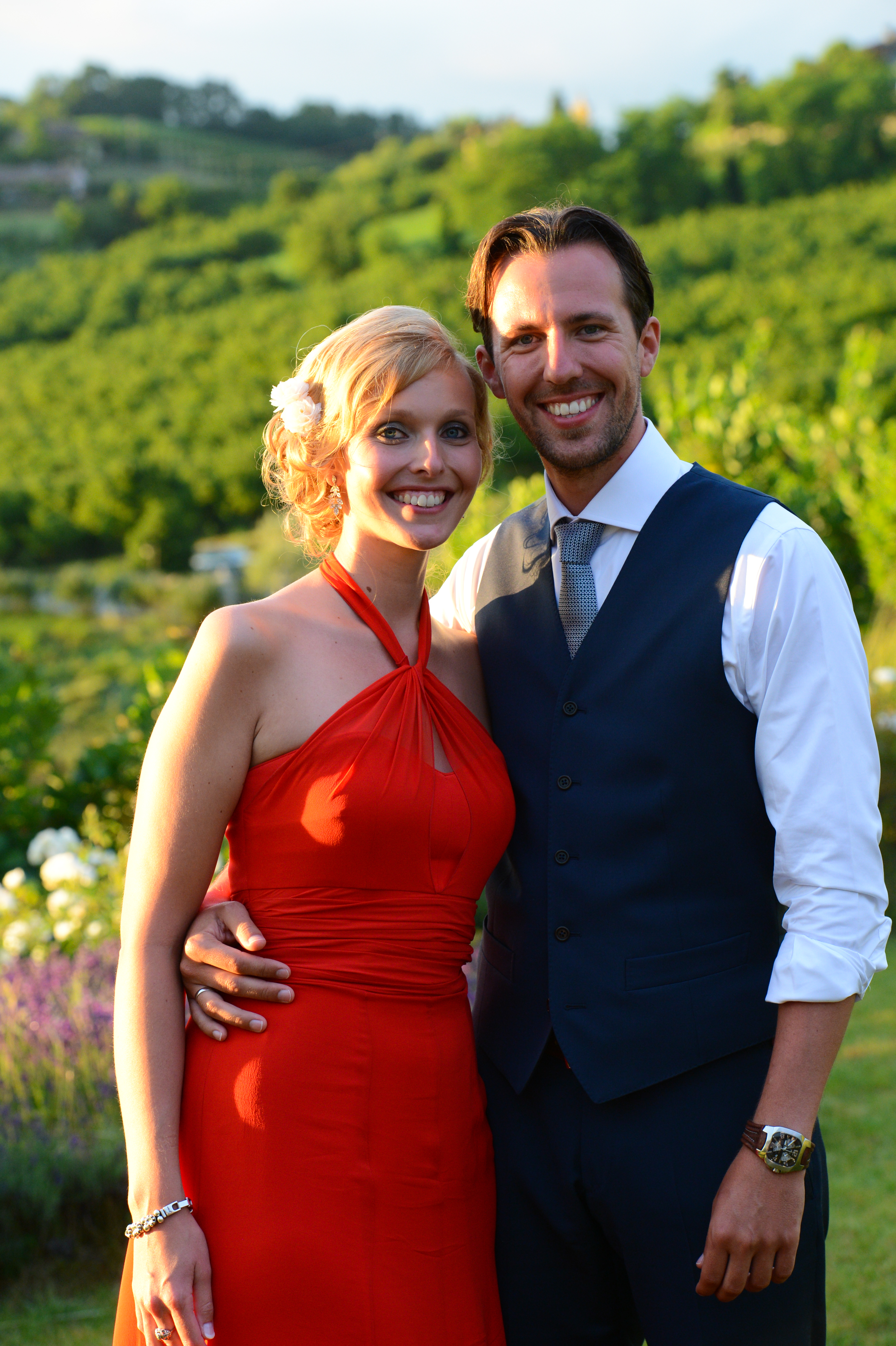 A smiling couple poses together at a wedding, with the man's arm around the woman's waist.