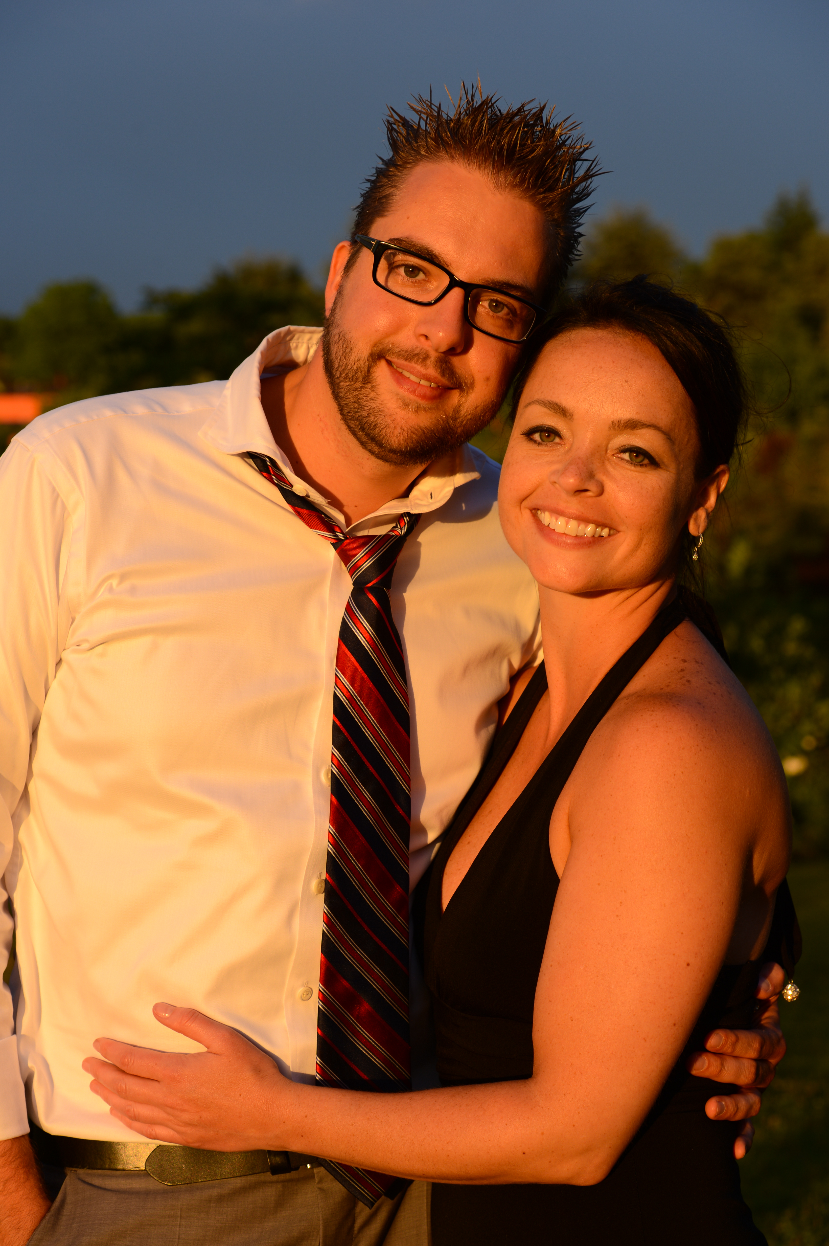 A smiling couple poses together at a wedding, embracing each other in warm sunlight.