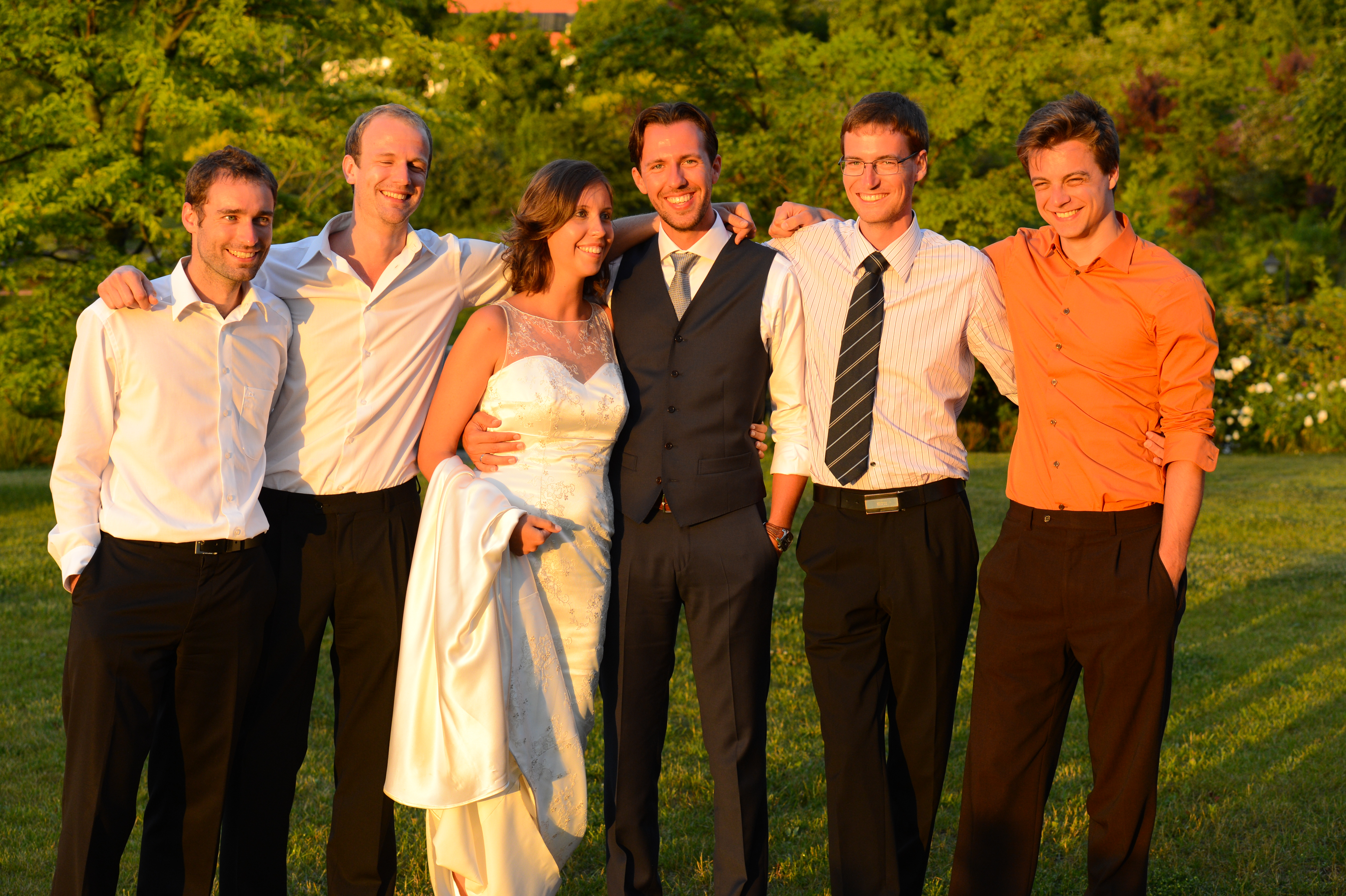 The bride and groom stand together, smiling with four friends in an outdoor setting during their wedding.