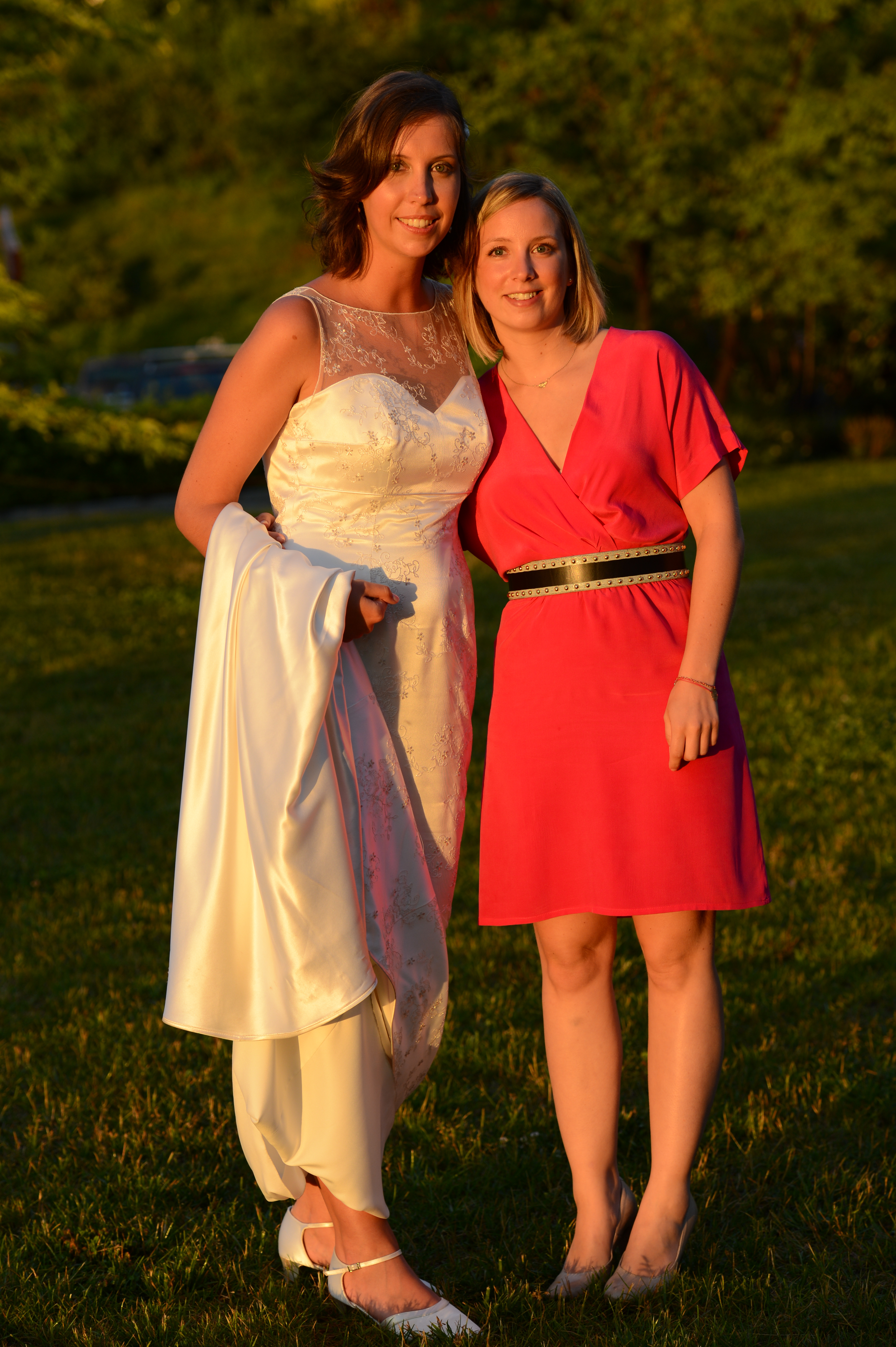 A bride in a white wedding dress stands next to a woman in a red dress, both smiling.