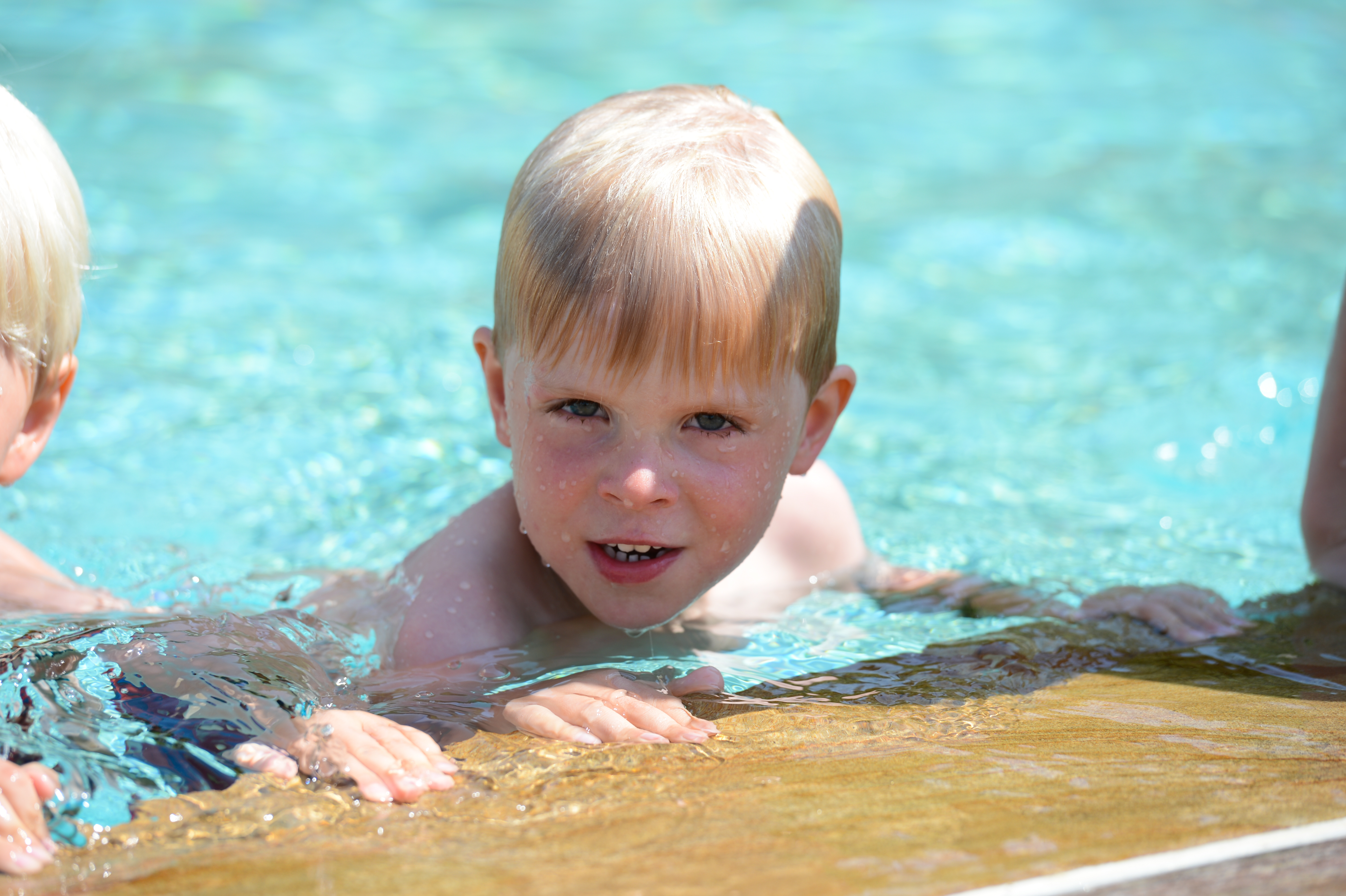 A young child with wet hair holds onto the pool edge, looking forward while swimming.