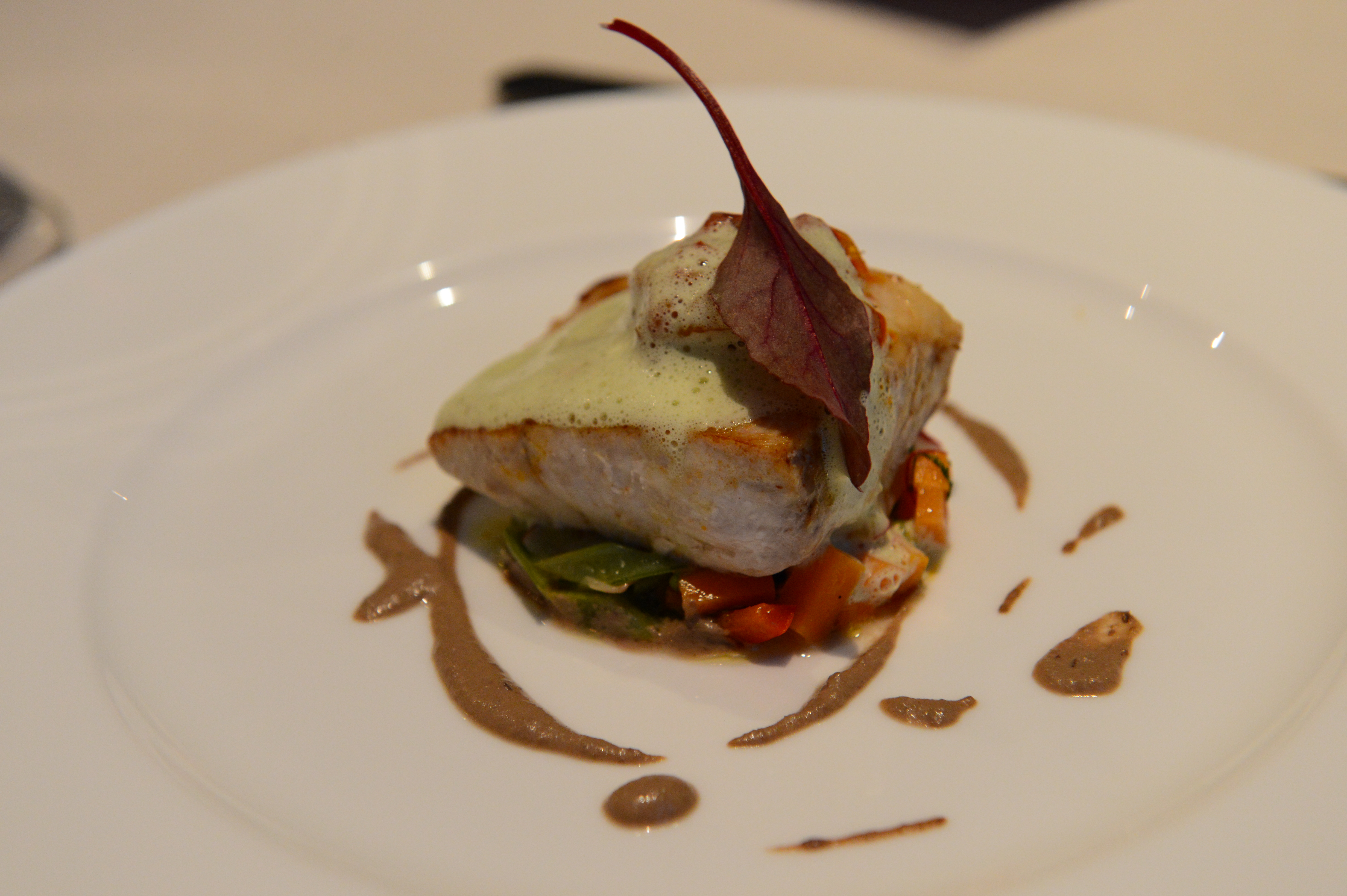 A plated gourmet dish with seared fish, vegetables, sauce, and a decorative leaf garnish at a wedding reception.