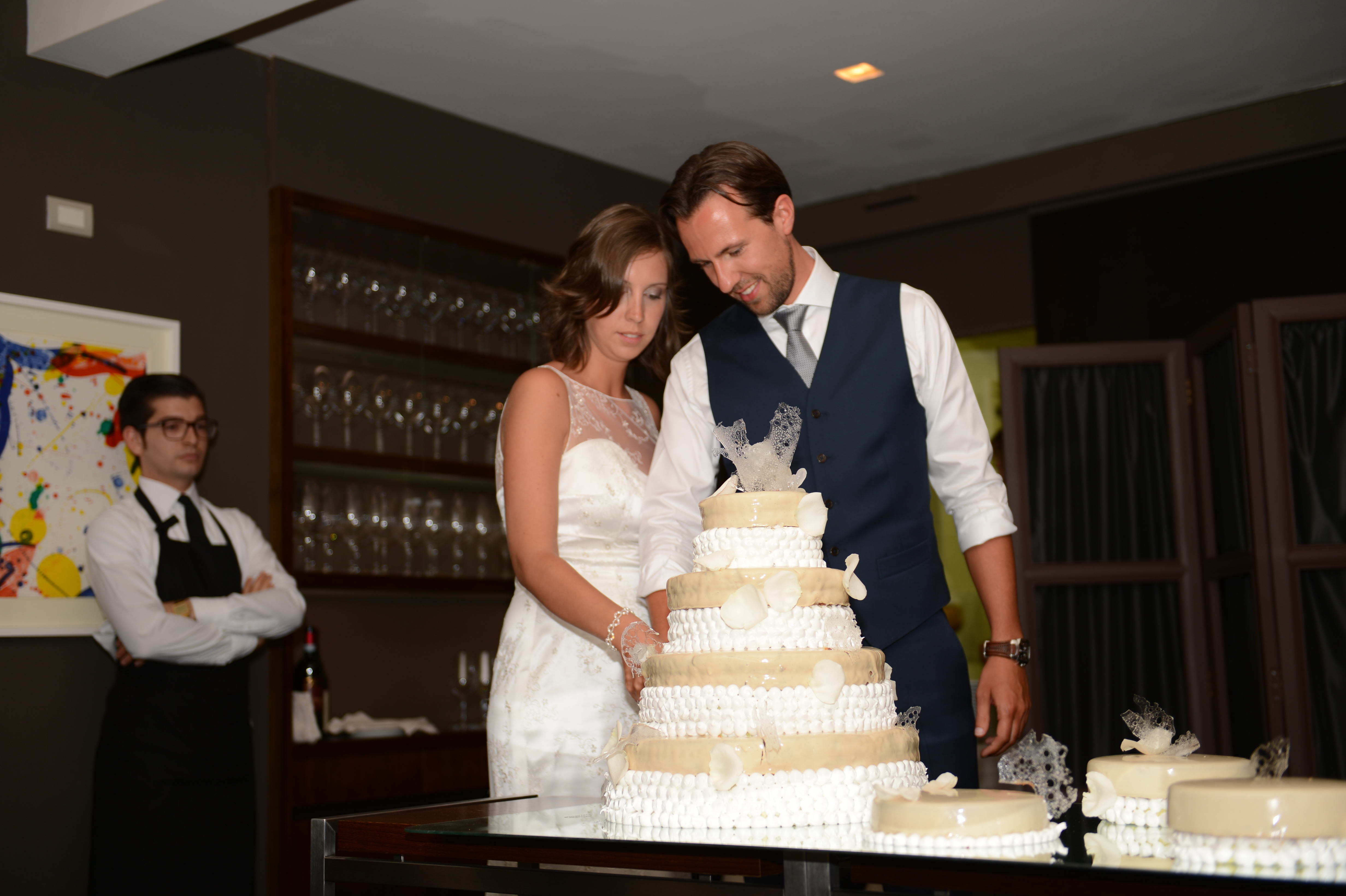 The bride and groom cut their wedding cake together, standing close and holding the knife.