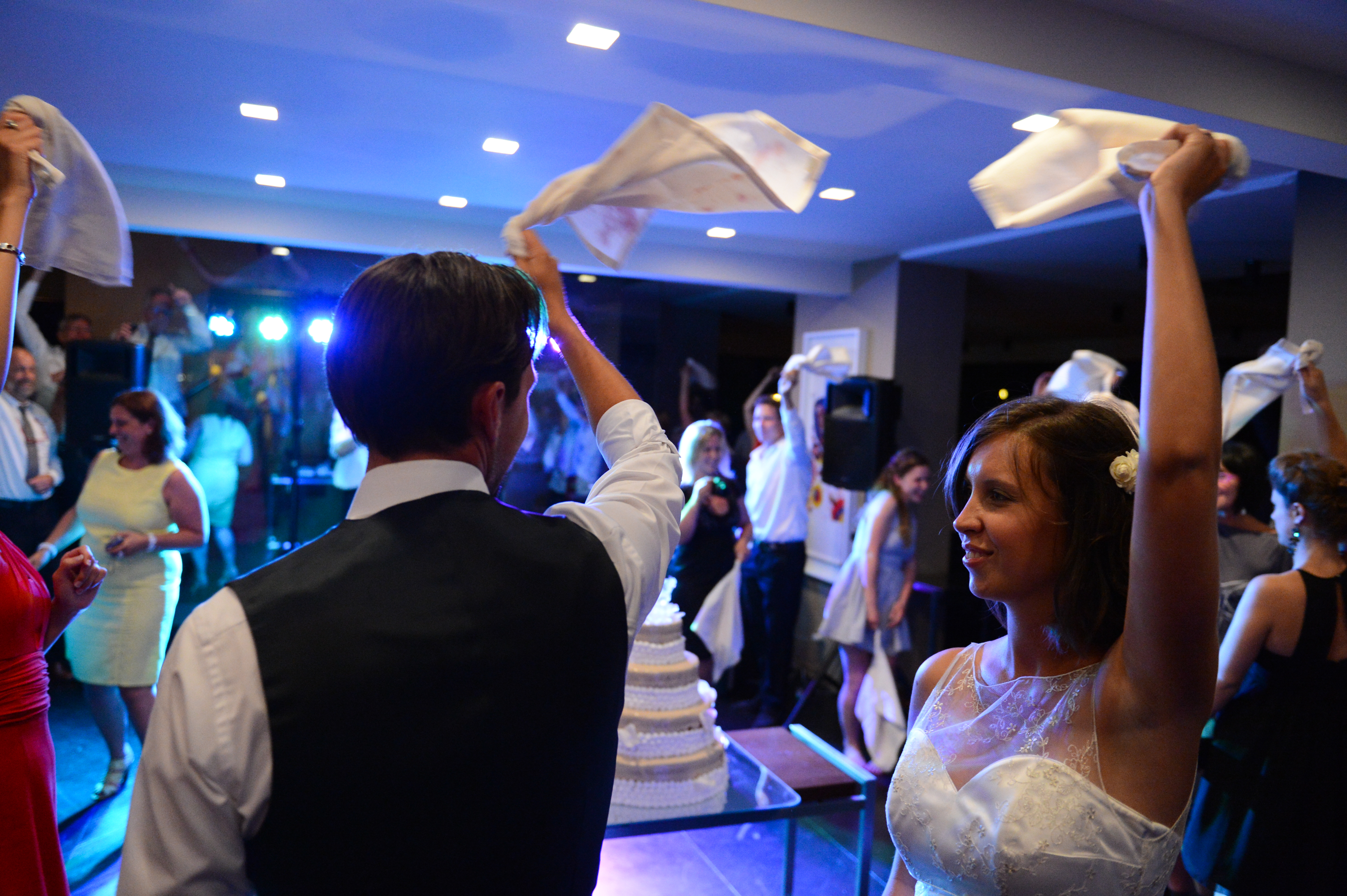 The bride and groom wave napkins in the air while guests celebrate around them at their wedding reception.