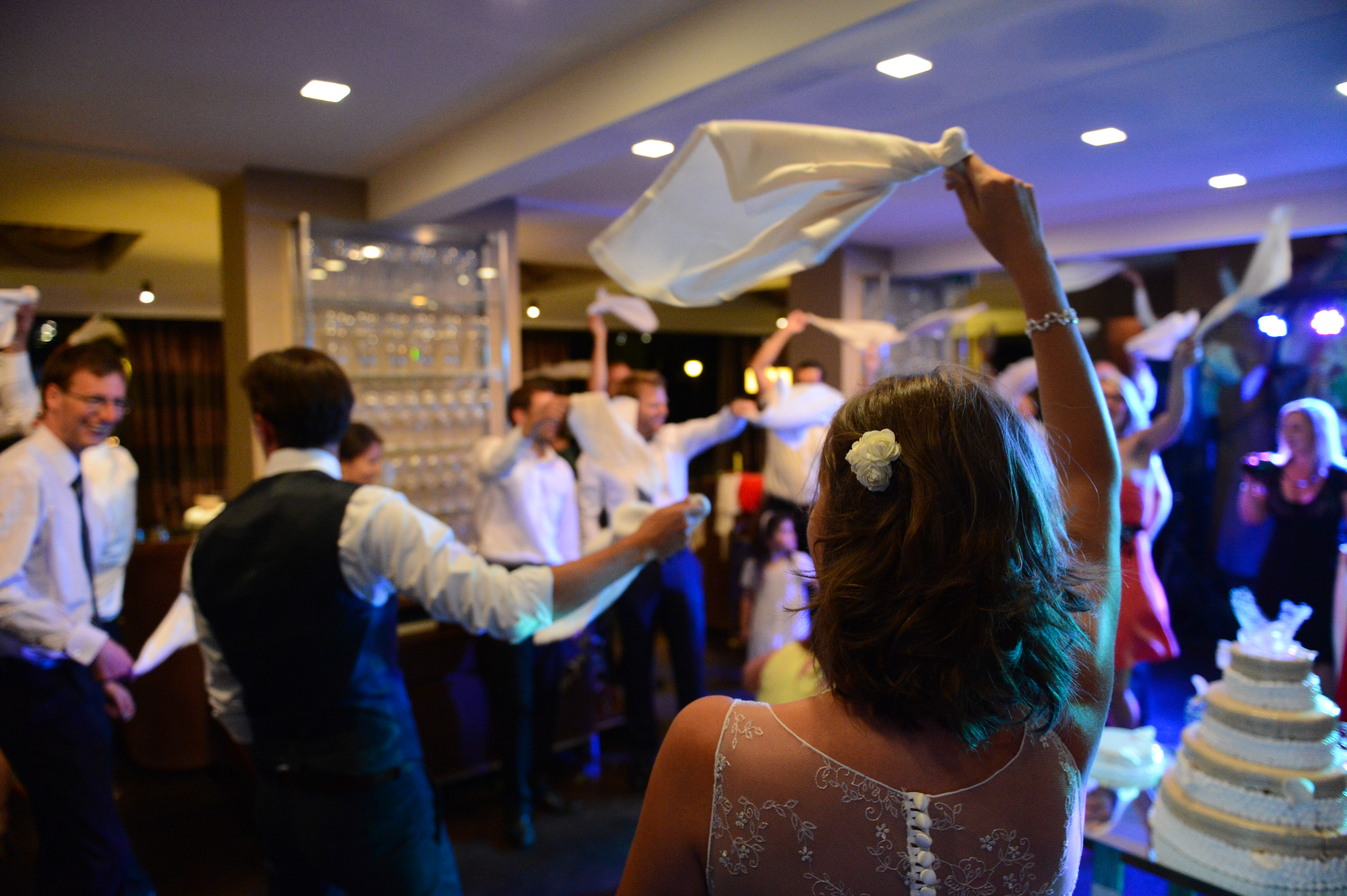 Wedding guests wave white napkins in the air while dancing, with the bride and groom in the foreground.