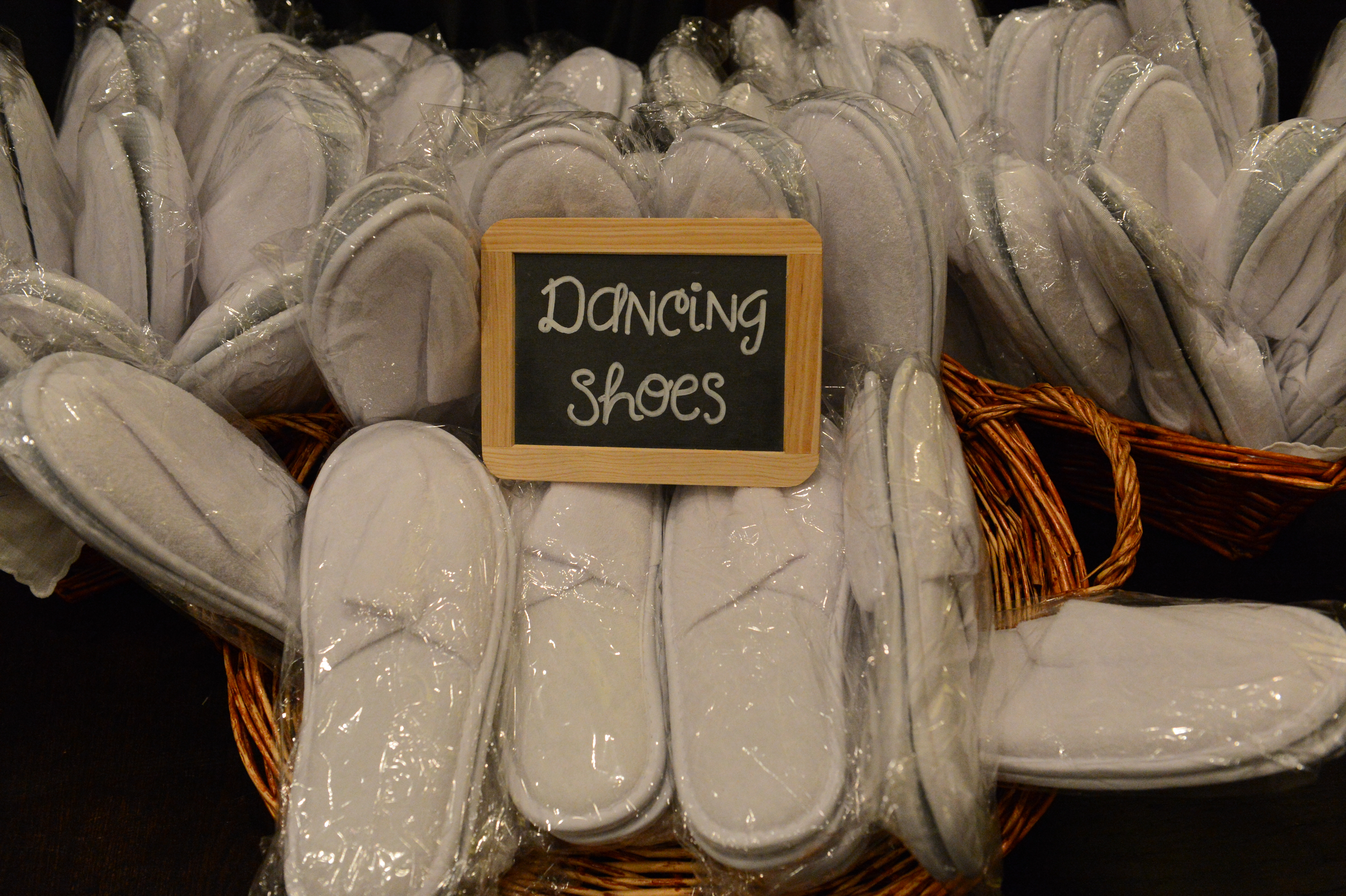 Baskets filled with white slippers labeled "Dancing Shoes" for wedding guests.