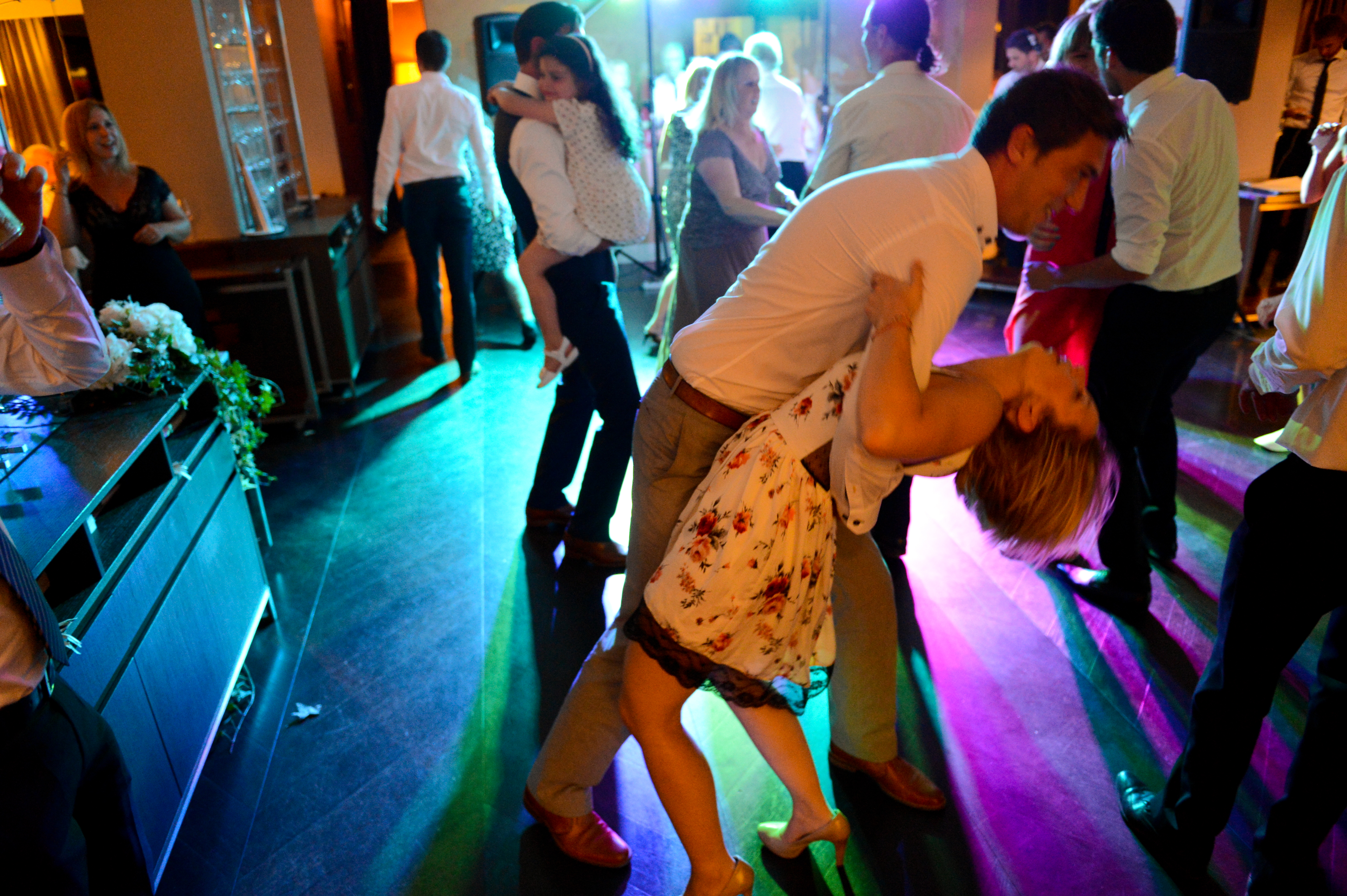 A couple dances energetically on the wedding dance floor, with the man dipping the woman backward.