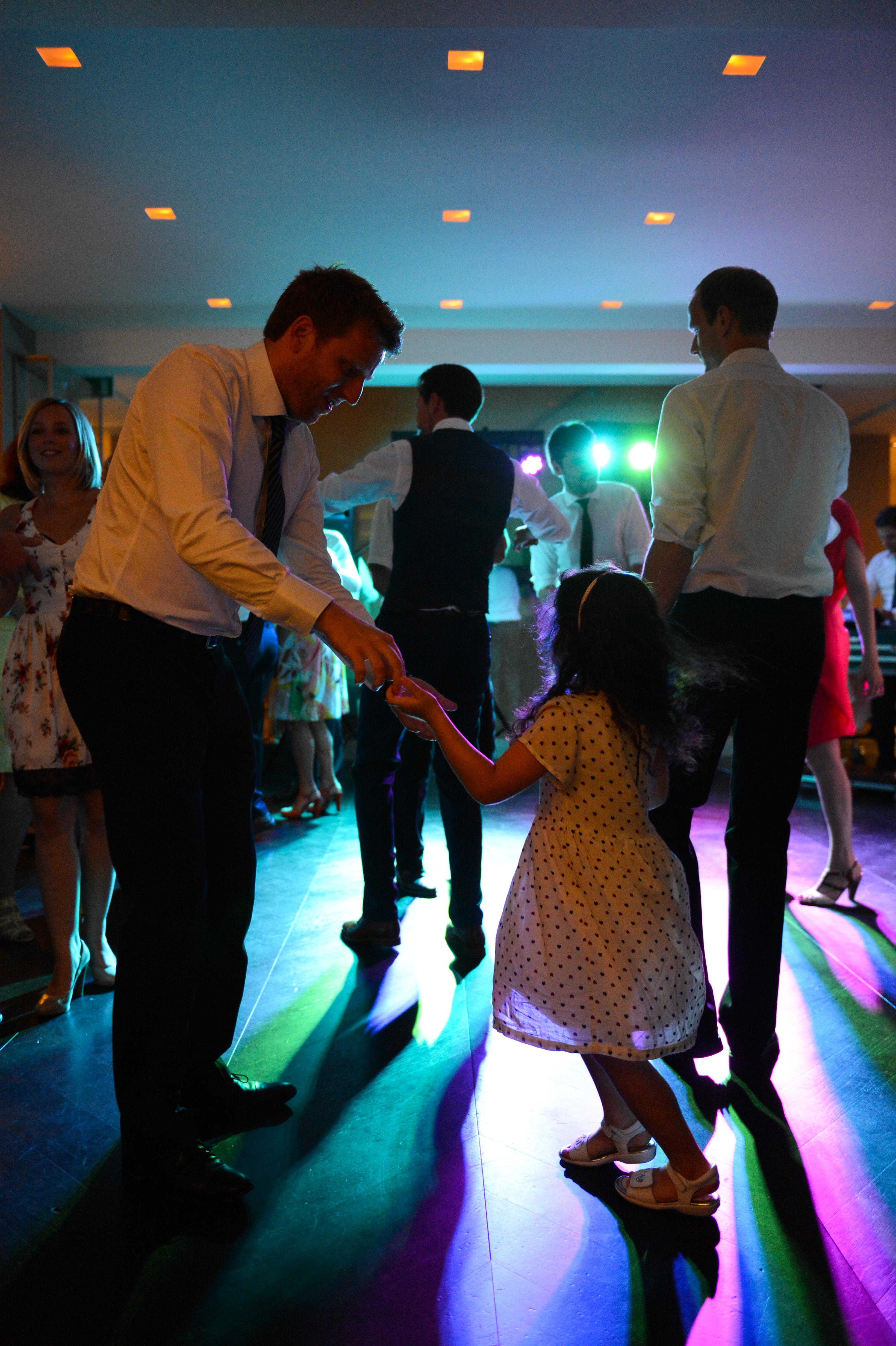 A man in a suit dances with a young girl in a polka-dot dress at a wedding reception.
