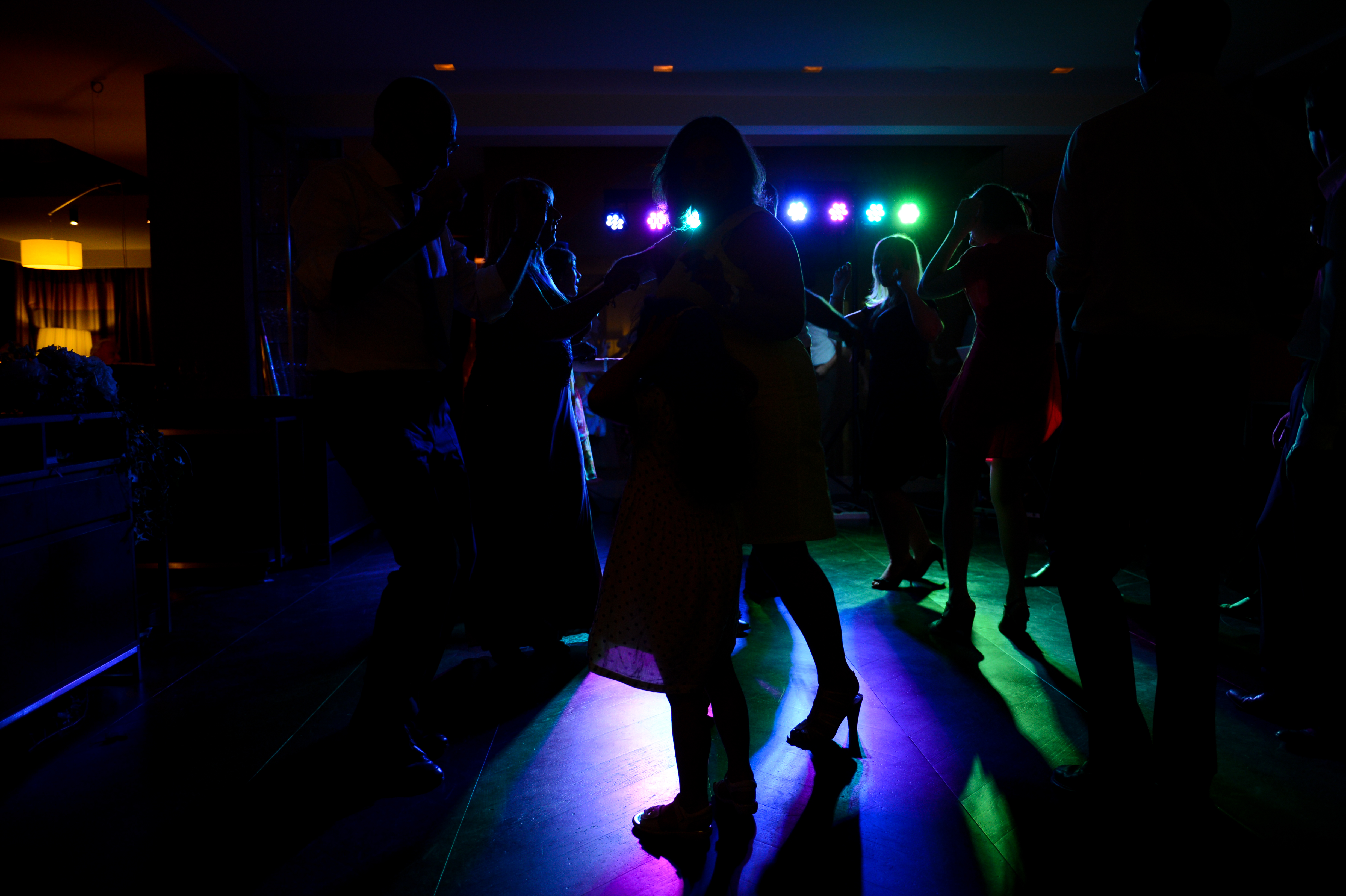 Wedding guests dancing in a dimly lit venue with colorful lights in the background.