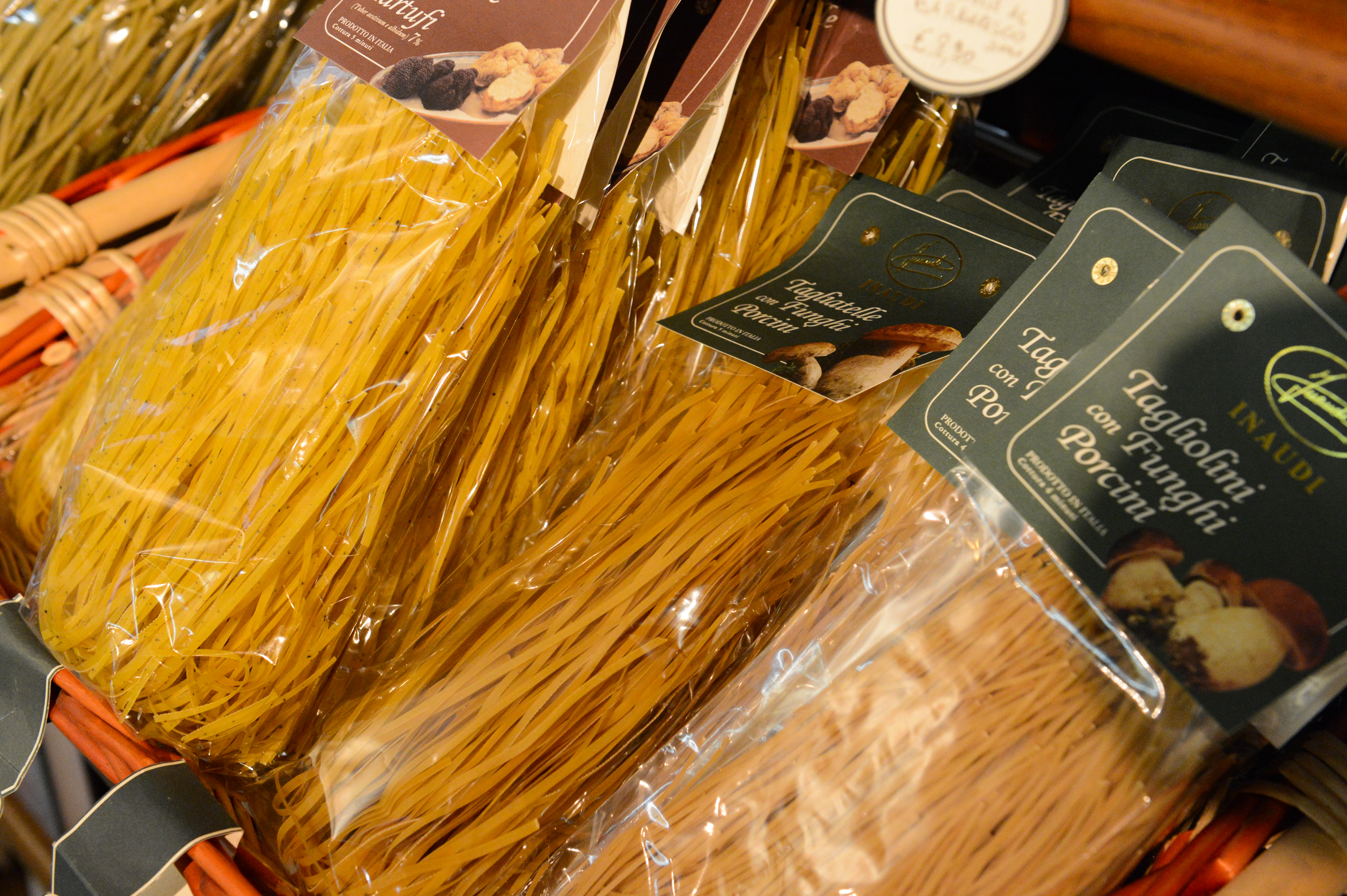 Bags of packaged tagliolini pasta with porcini mushrooms displayed in a basket at a store.