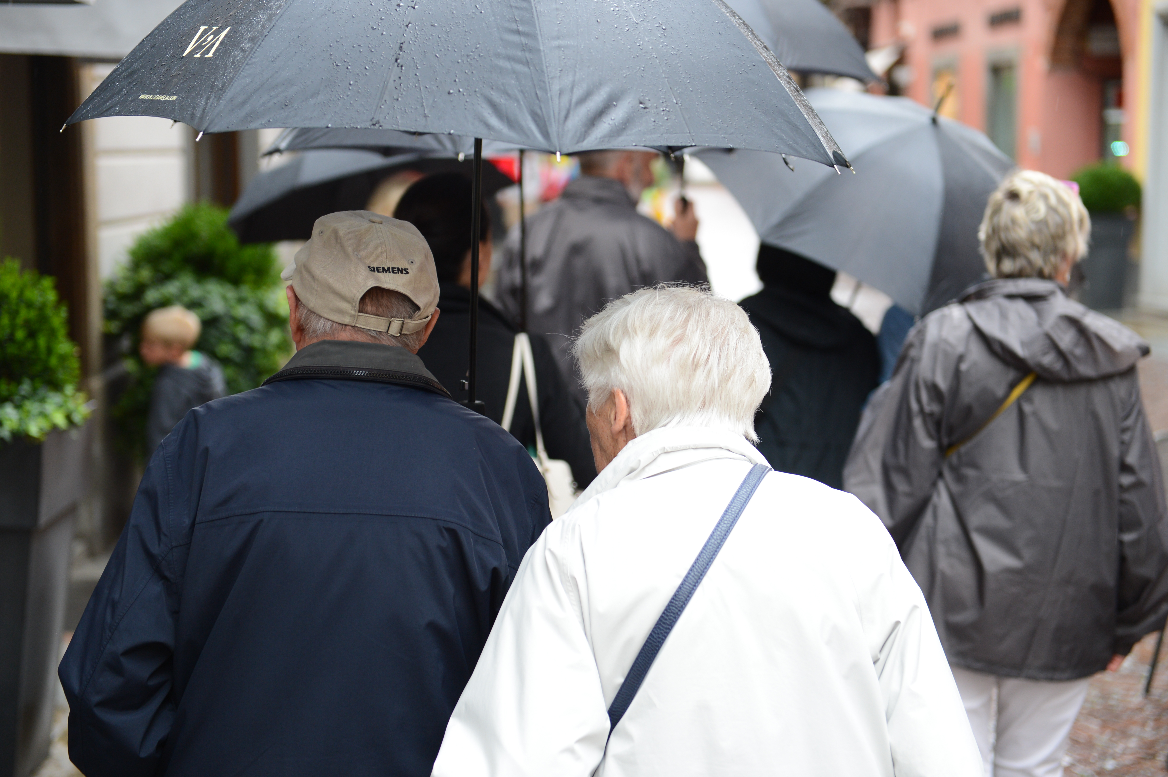 A group of people walking in the rain with umbrellas, including an elderly couple in the foreground.