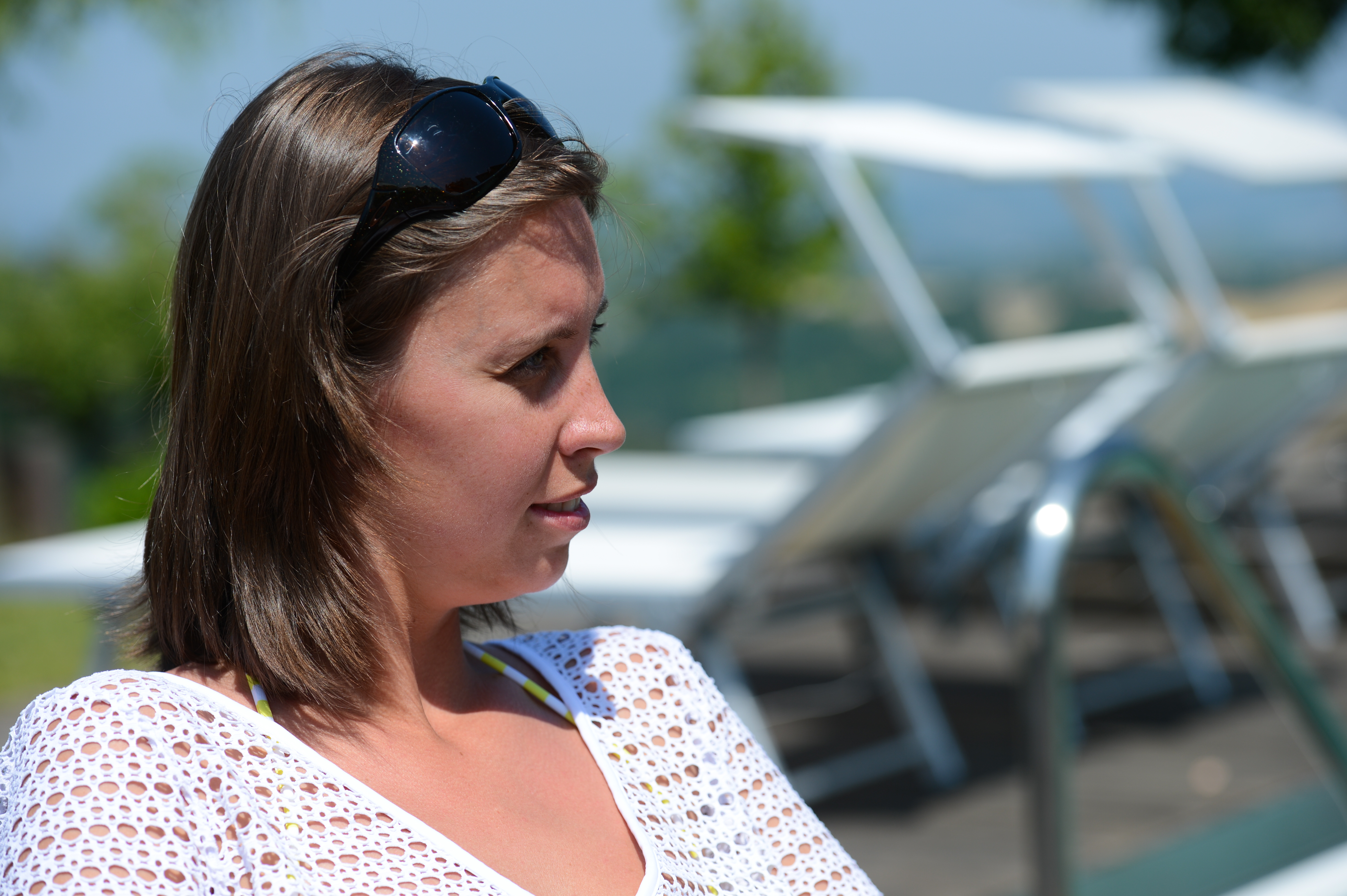 A woman wearing sunglasses on her head sits outdoors, looking to the side with a relaxed expression.