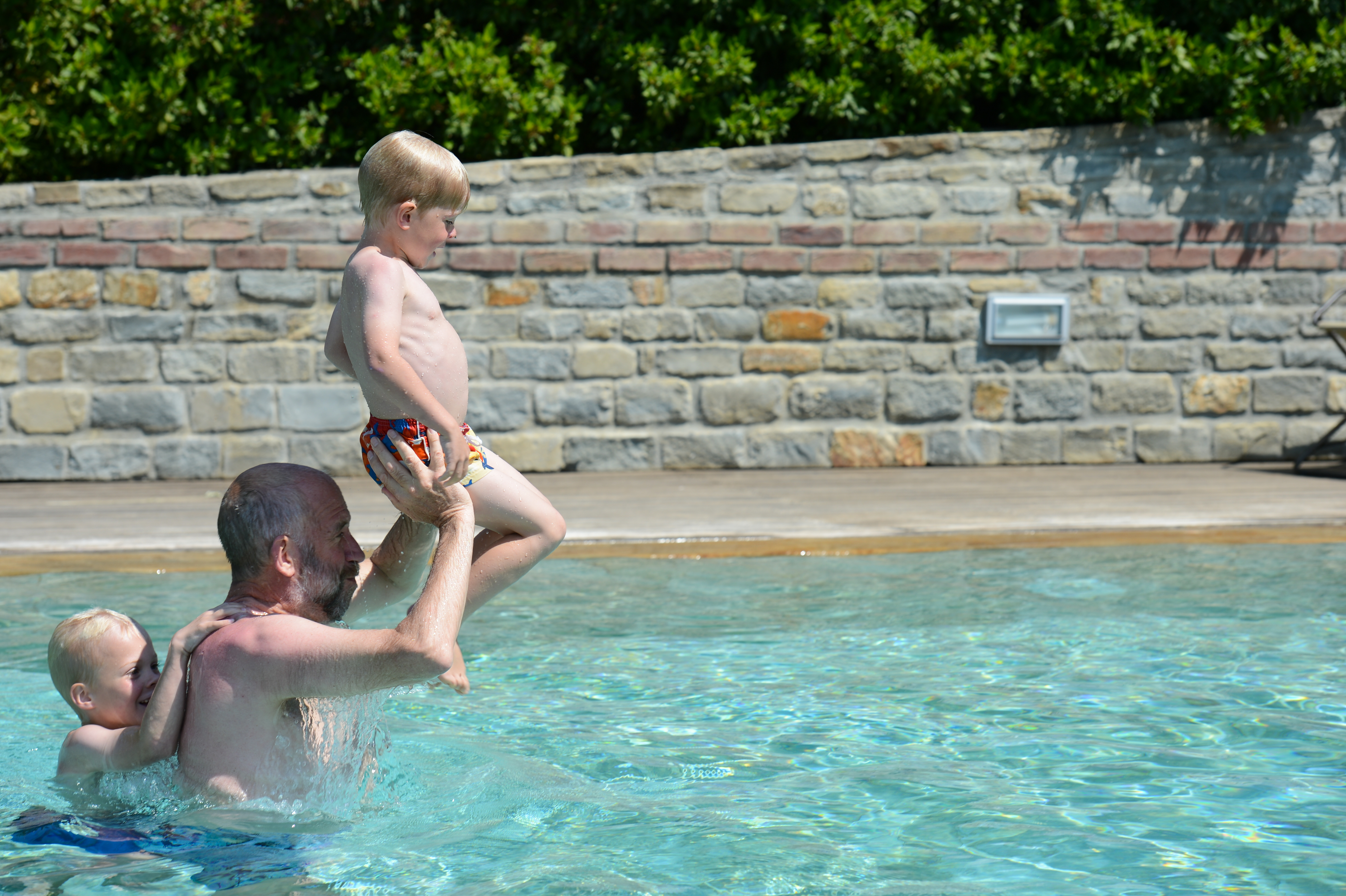 A man in a pool lifts a young child while another child holds onto his back.