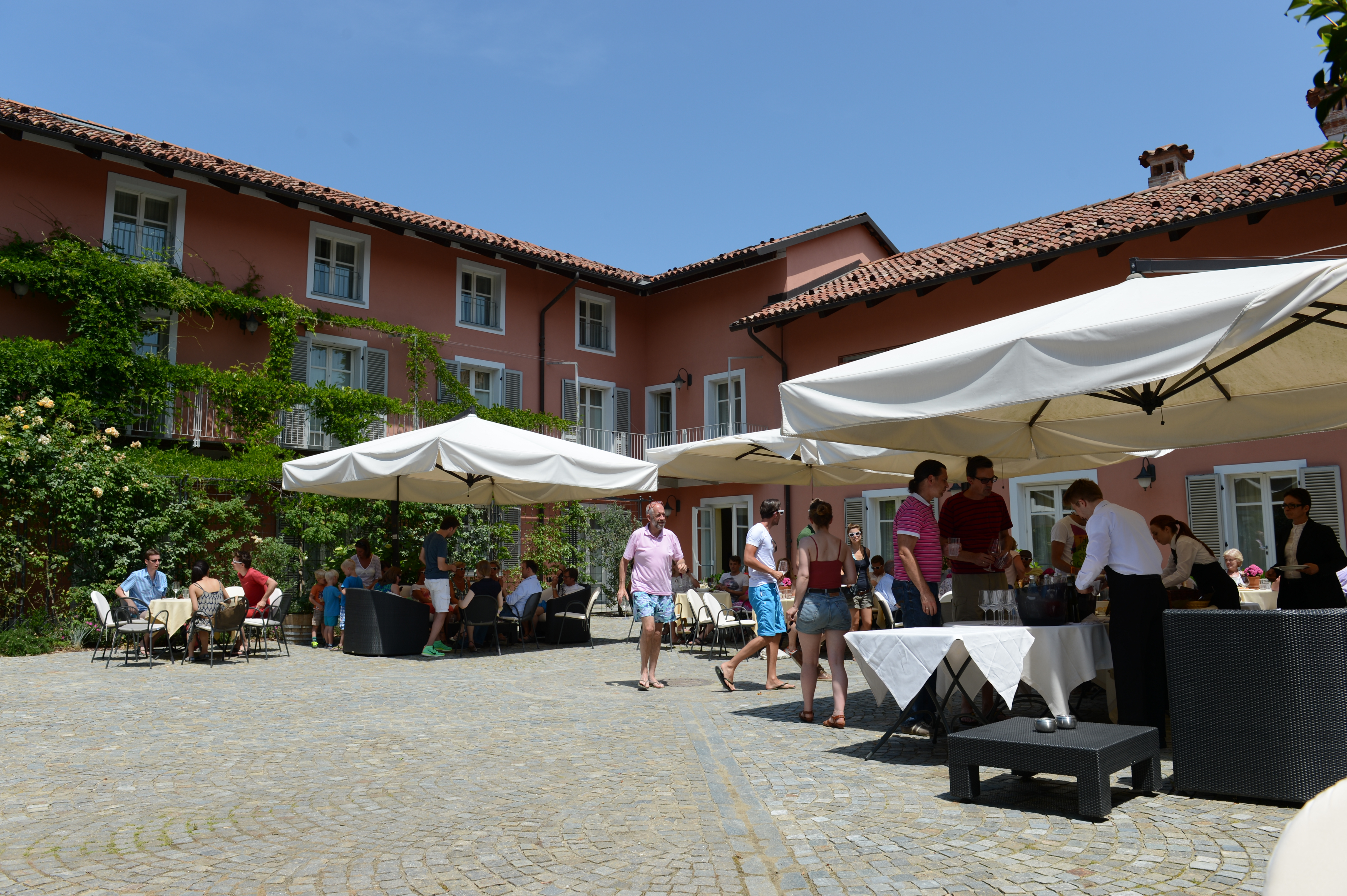 Guests gather outdoors under umbrellas, enjoying drinks and conversation at a wedding reception in a courtyard.