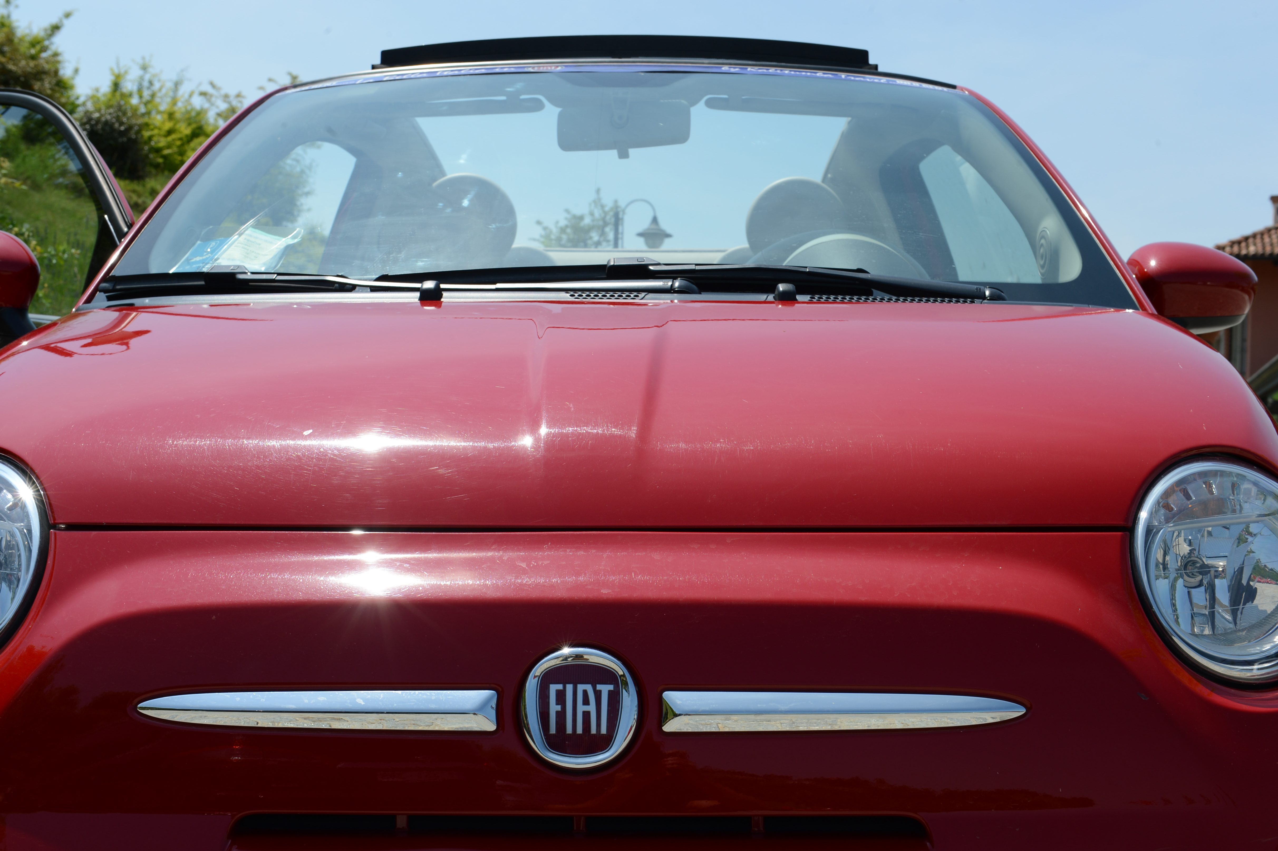 Close-up of a red Fiat car with an open door, parked outdoors on a sunny day.