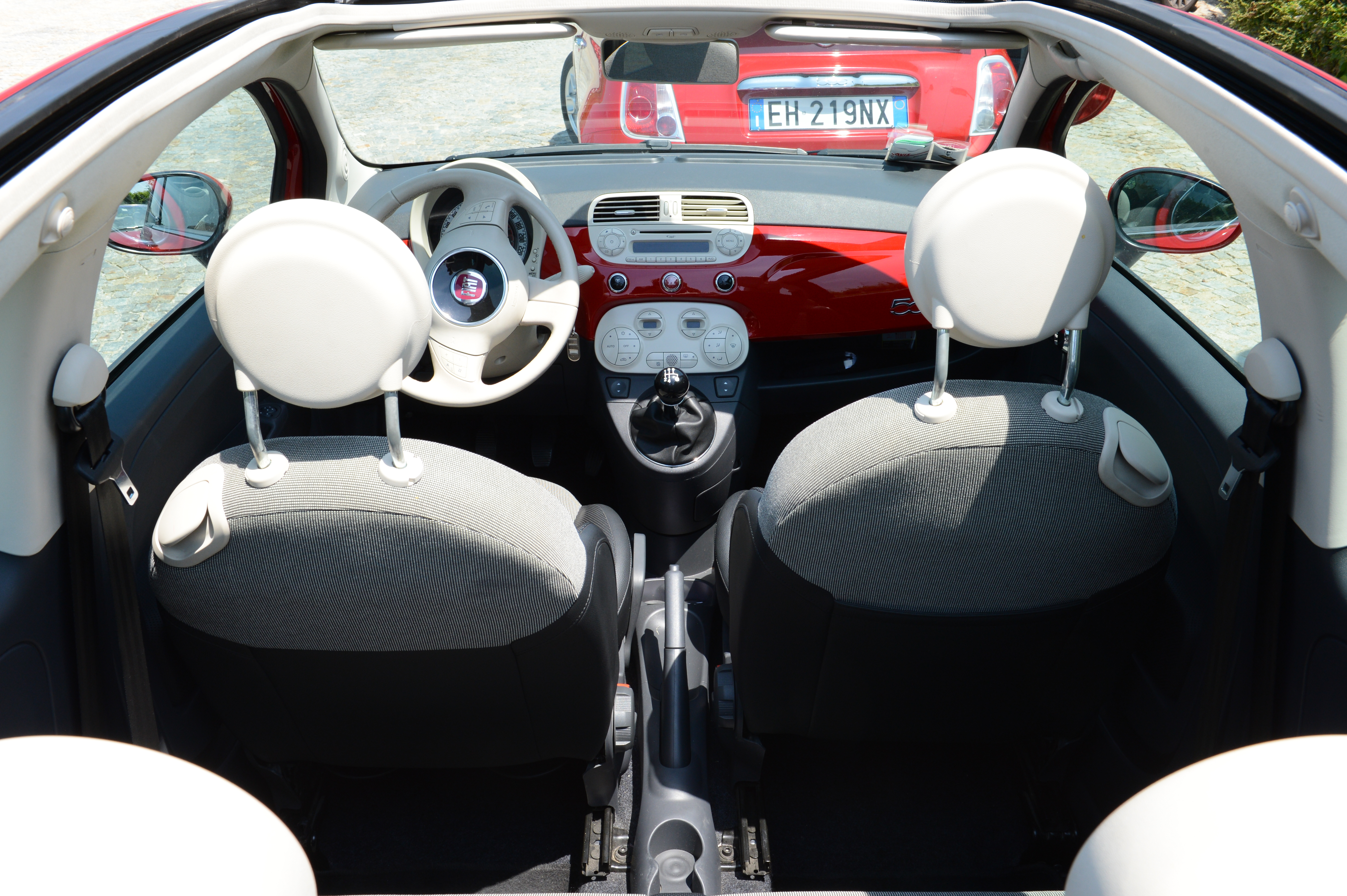 View of a small convertible car's interior from the back, showing the dashboard, steering wheel, and front seats.