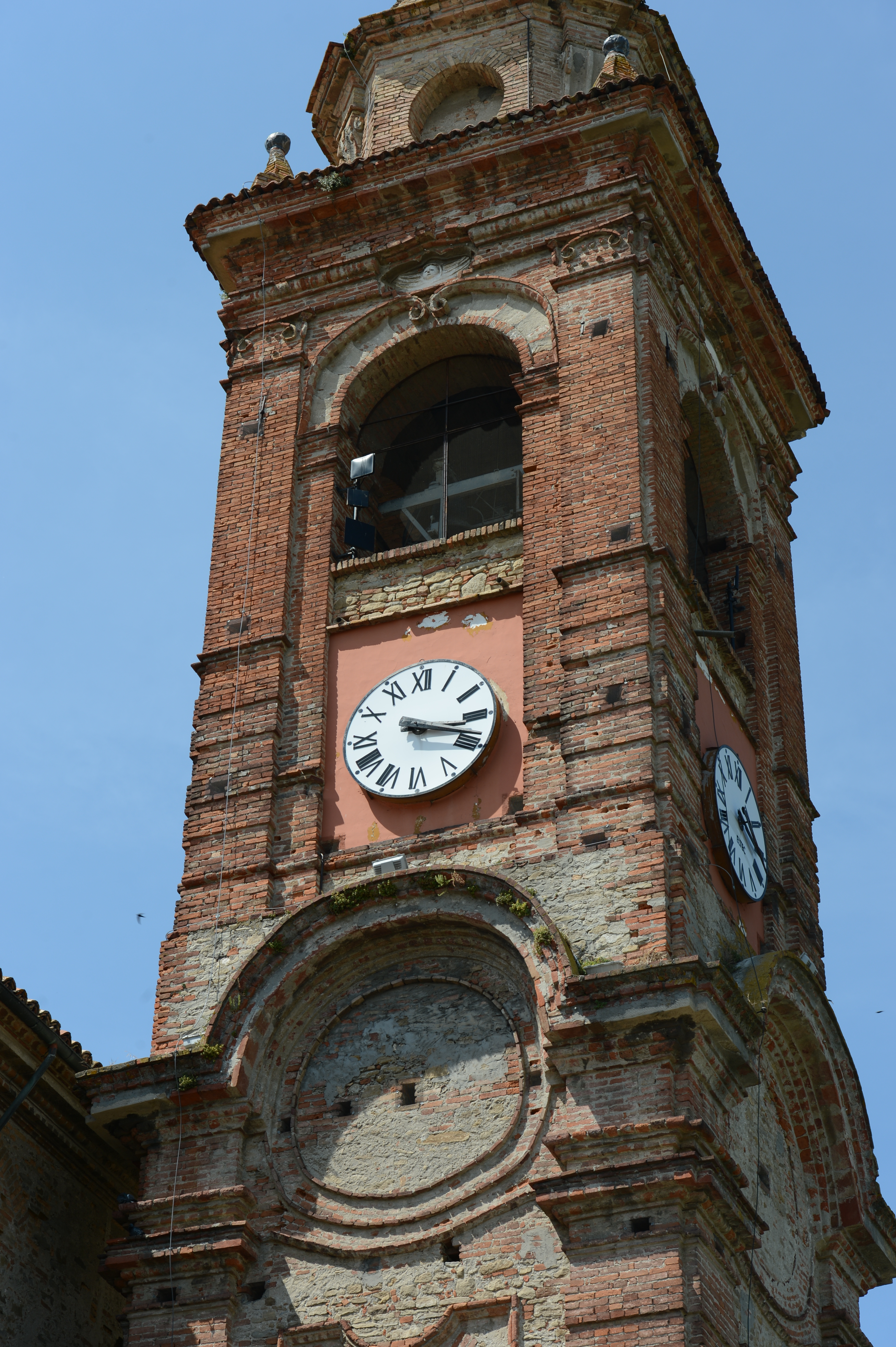 A tall brick clock tower with two visible clock faces, showing the time against a clear blue sky.