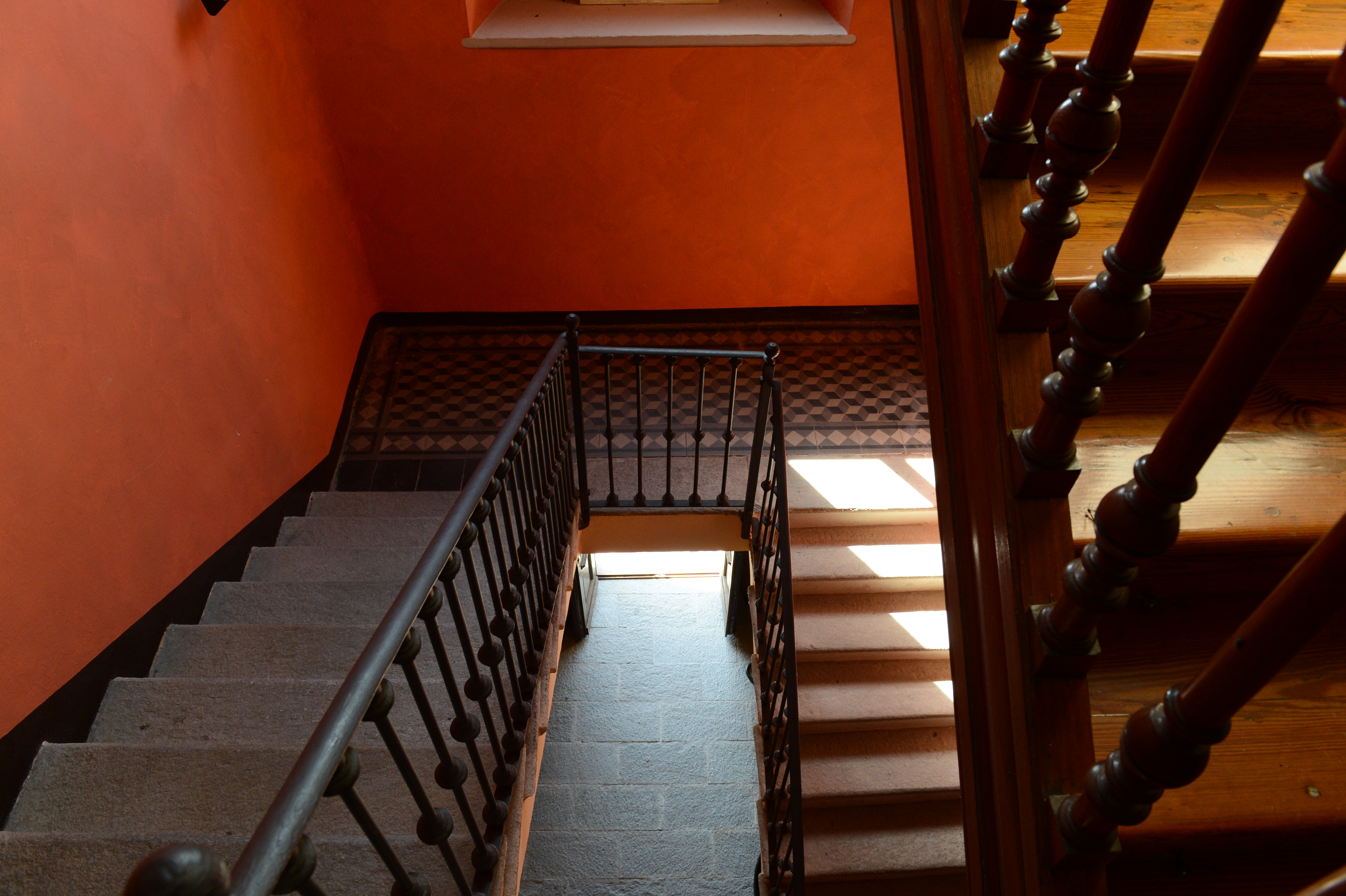 A staircase with black railings and wooden steps in a warmly lit interior with orange walls.