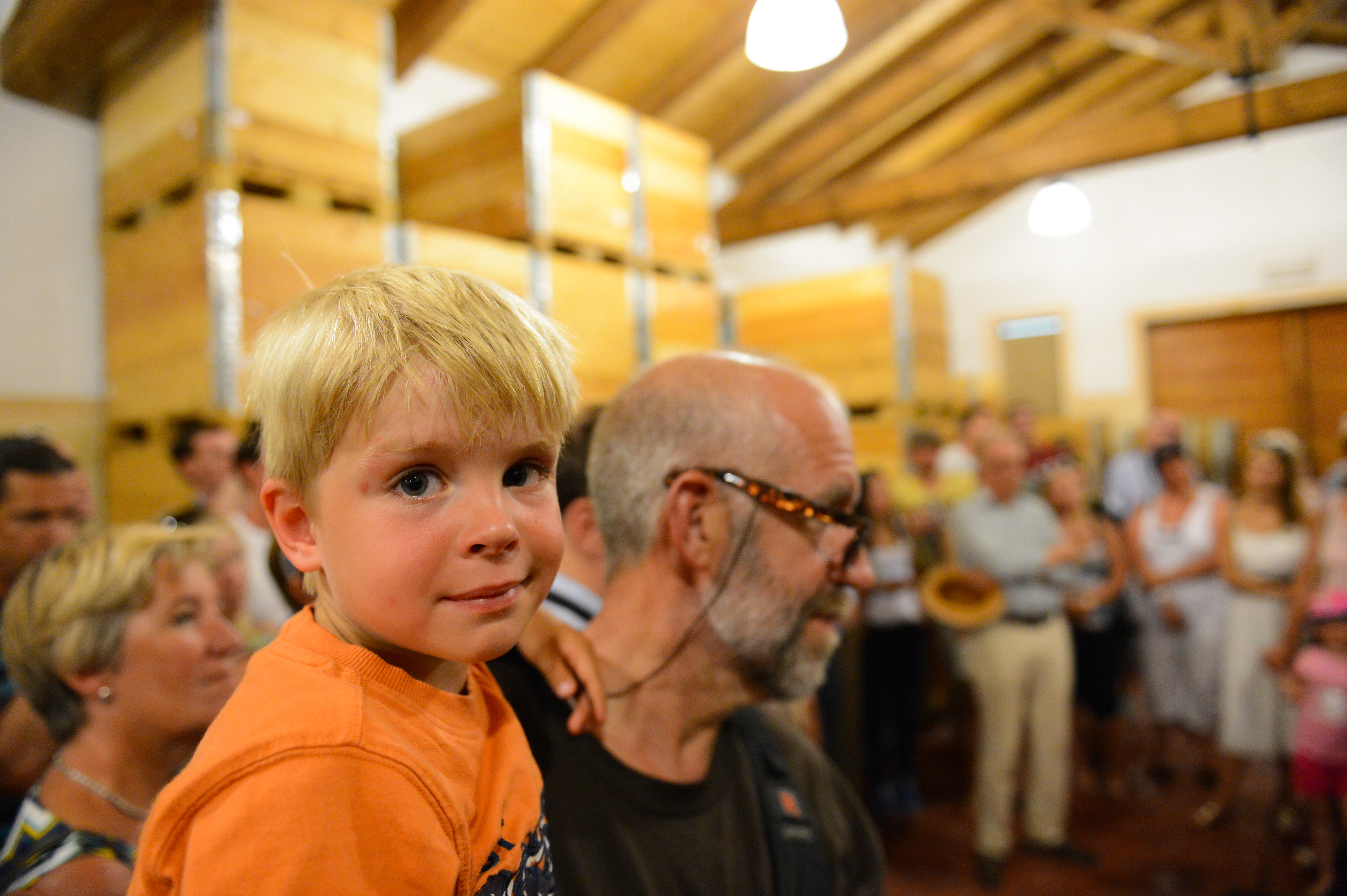 A young boy in an orange shirt sits on an older man's shoulders at a wedding reception.