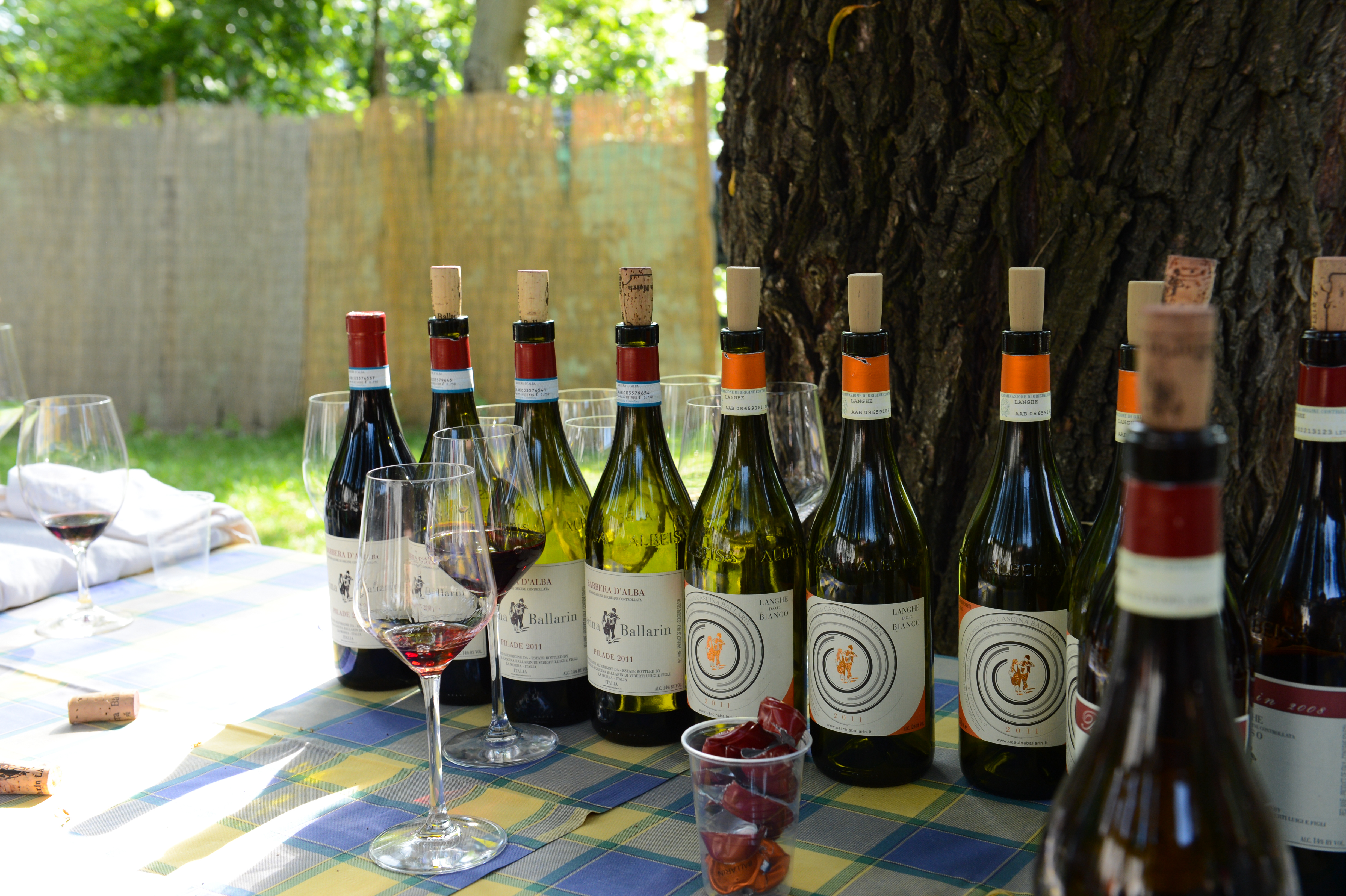 A table with several bottles of wine, glasses with red wine, and a cup with wrapped candies at a wedding.