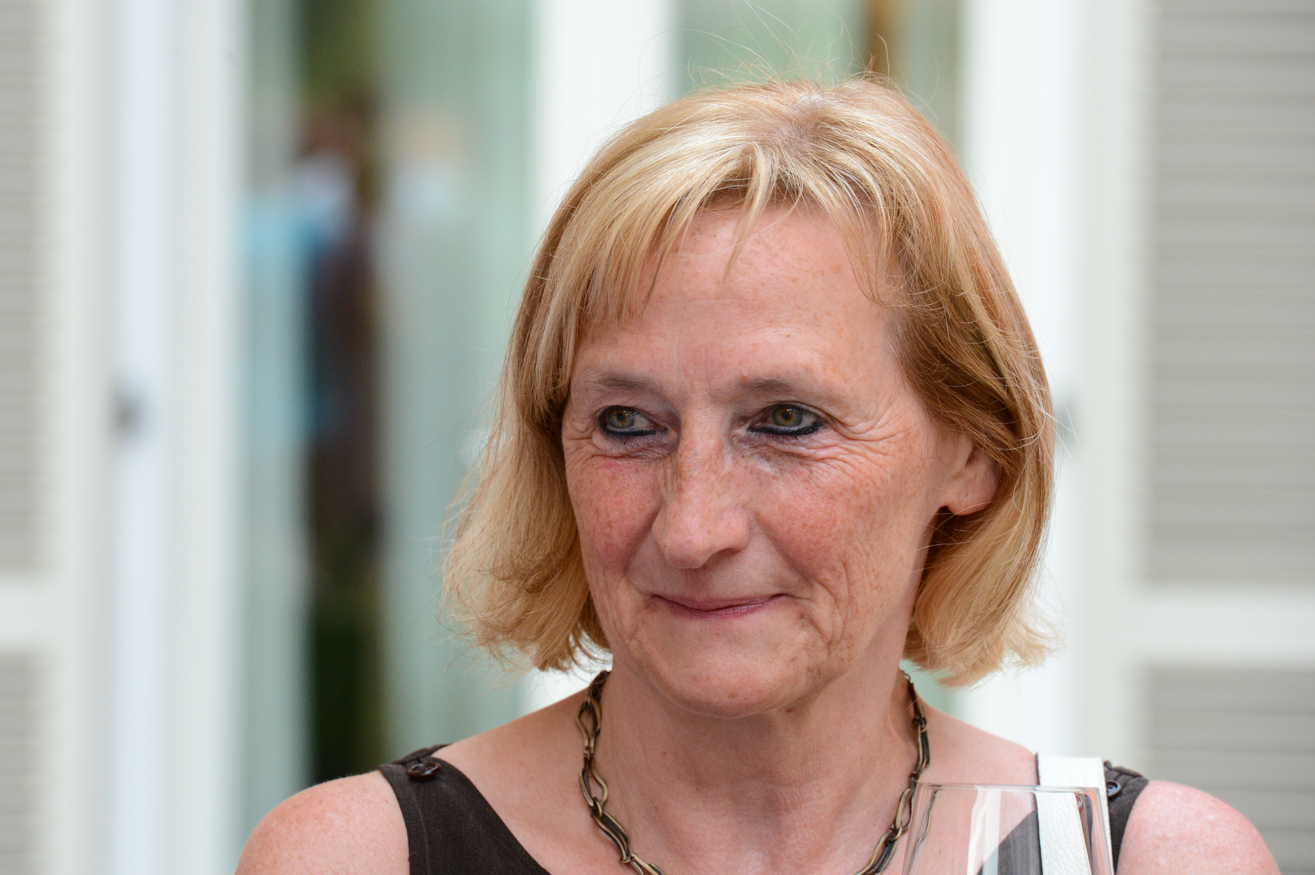 A woman with short blonde hair holds a glass and smiles at a wedding reception.