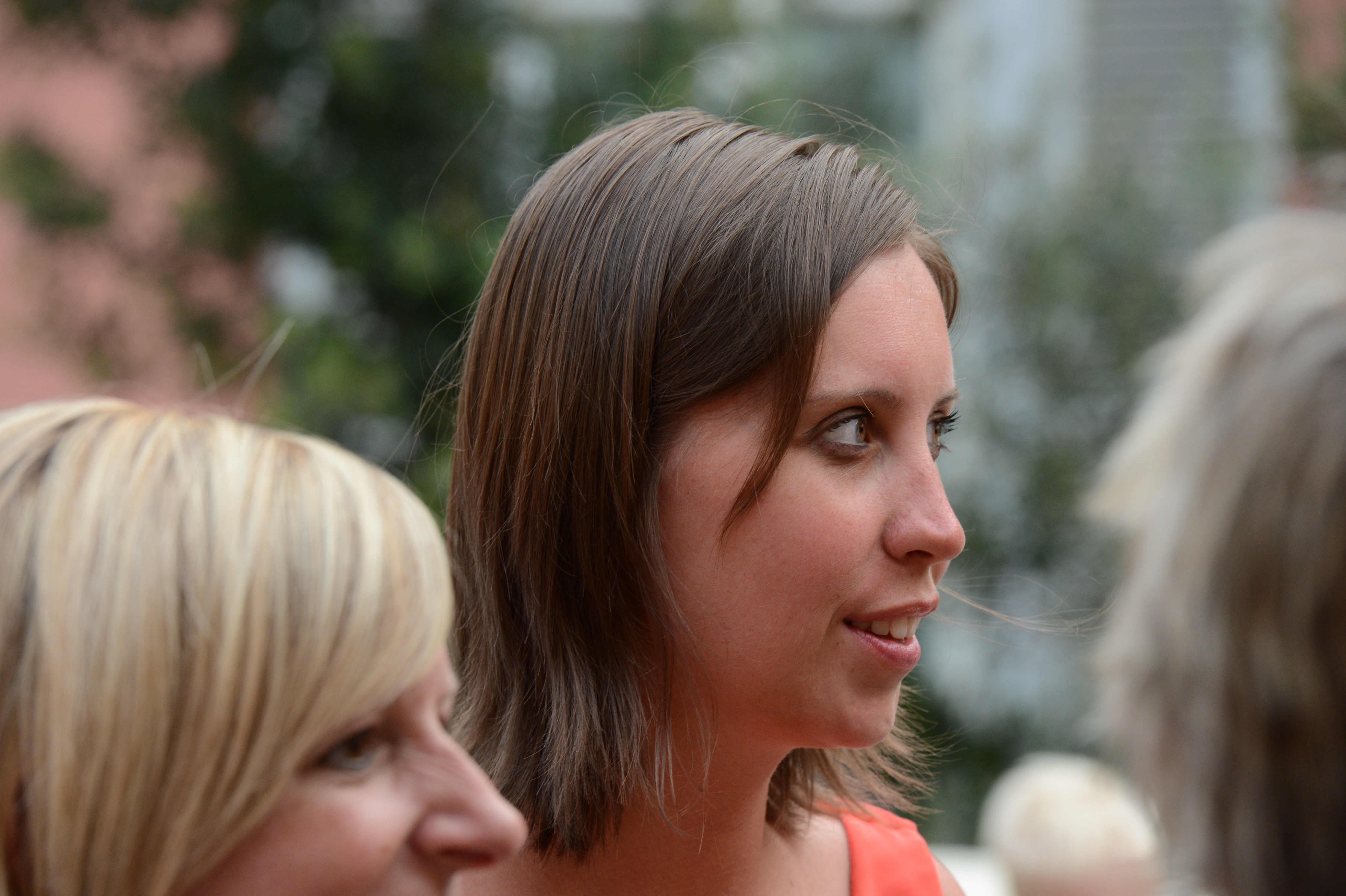 A woman in an orange dress is engaged in conversation at an outdoor wedding gathering.
