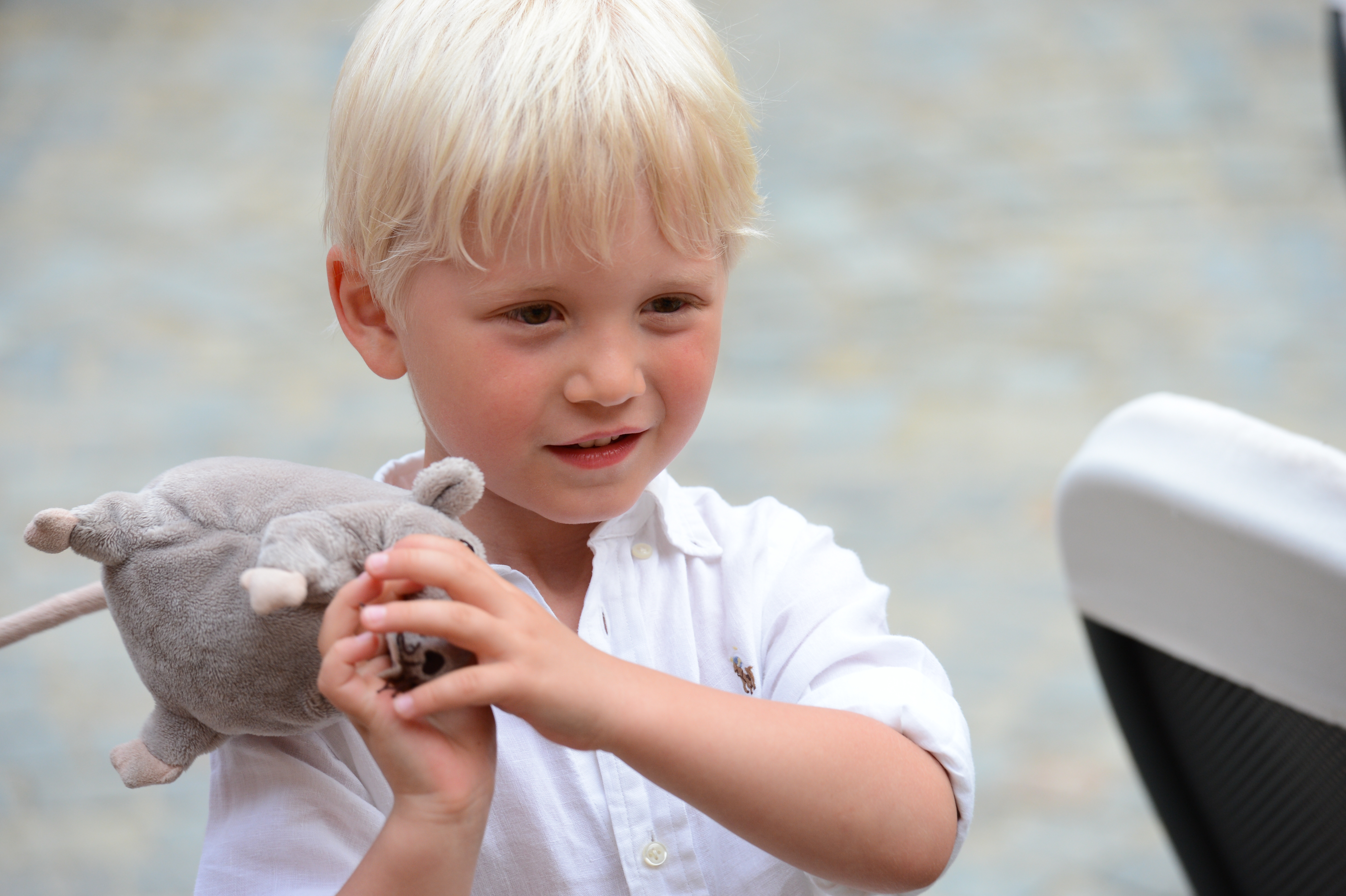 A young boy in a white shirt holds a stuffed animal and a small object, looking focused.