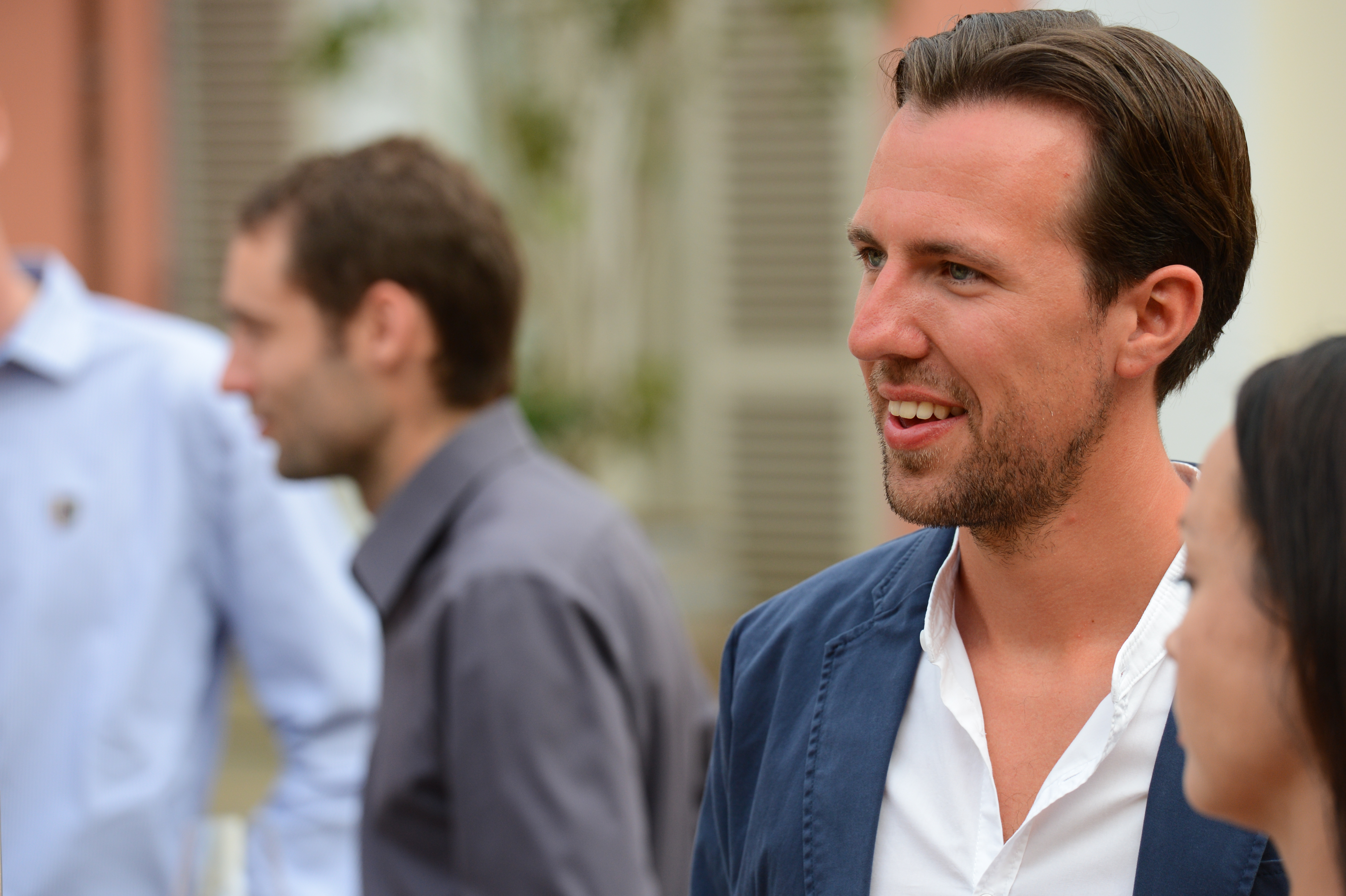 A man in a blue jacket smiles while talking to a woman at a wedding reception.