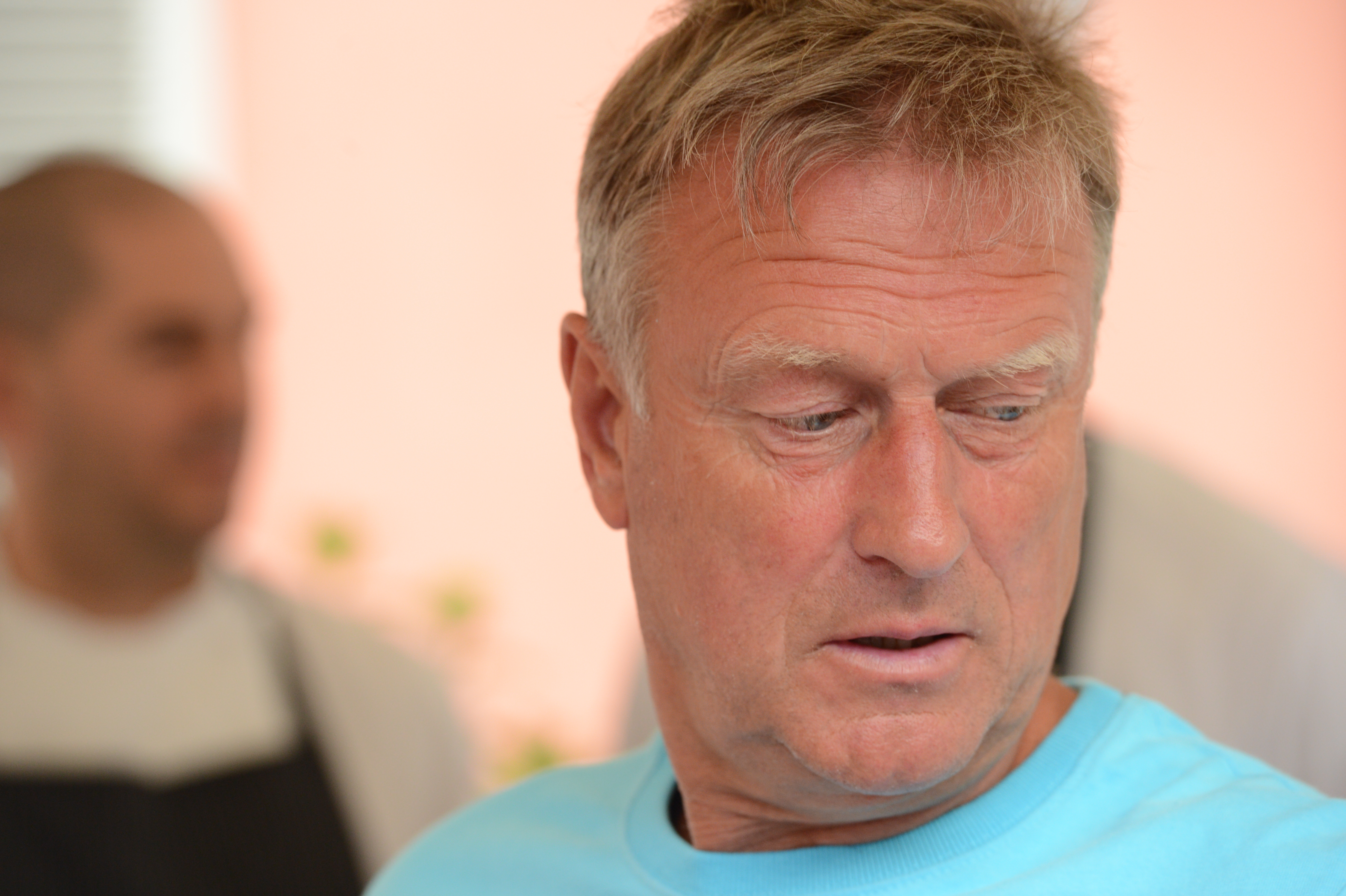 A man in a blue shirt looks to the side with a neutral expression.