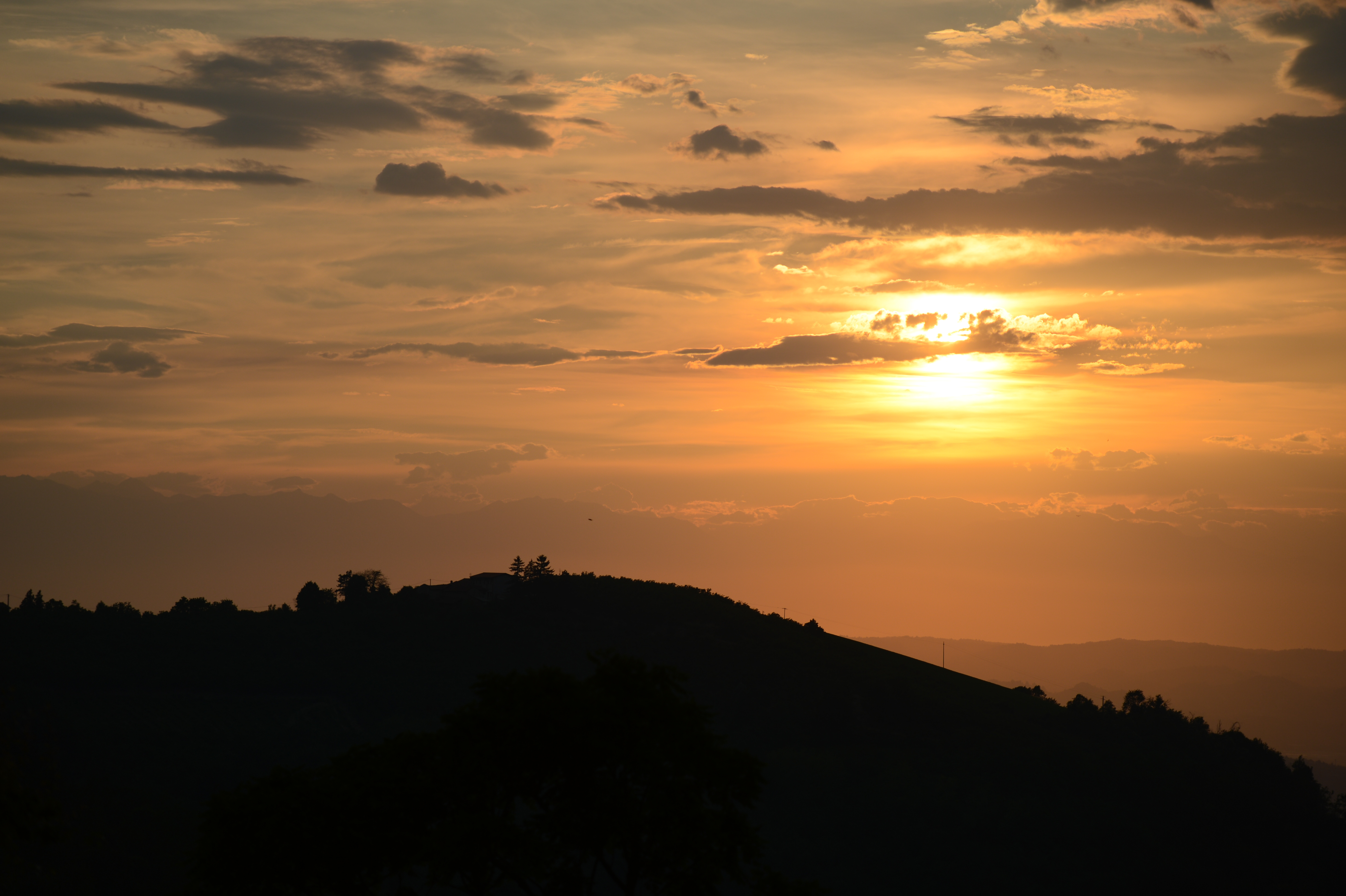 A sunset over rolling hills with scattered clouds in the sky.