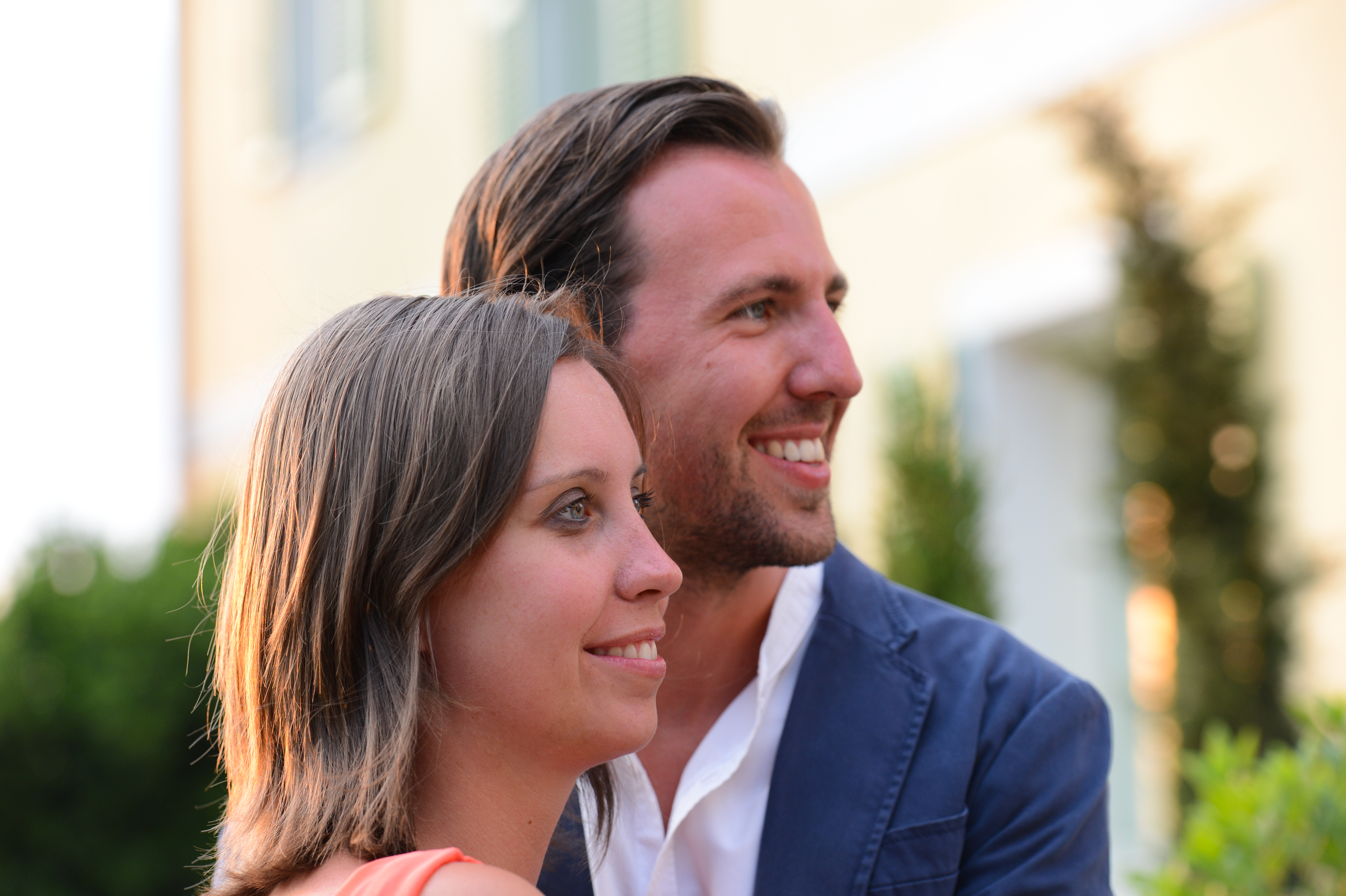 A smiling couple looks in the same direction at an outdoor wedding celebration.