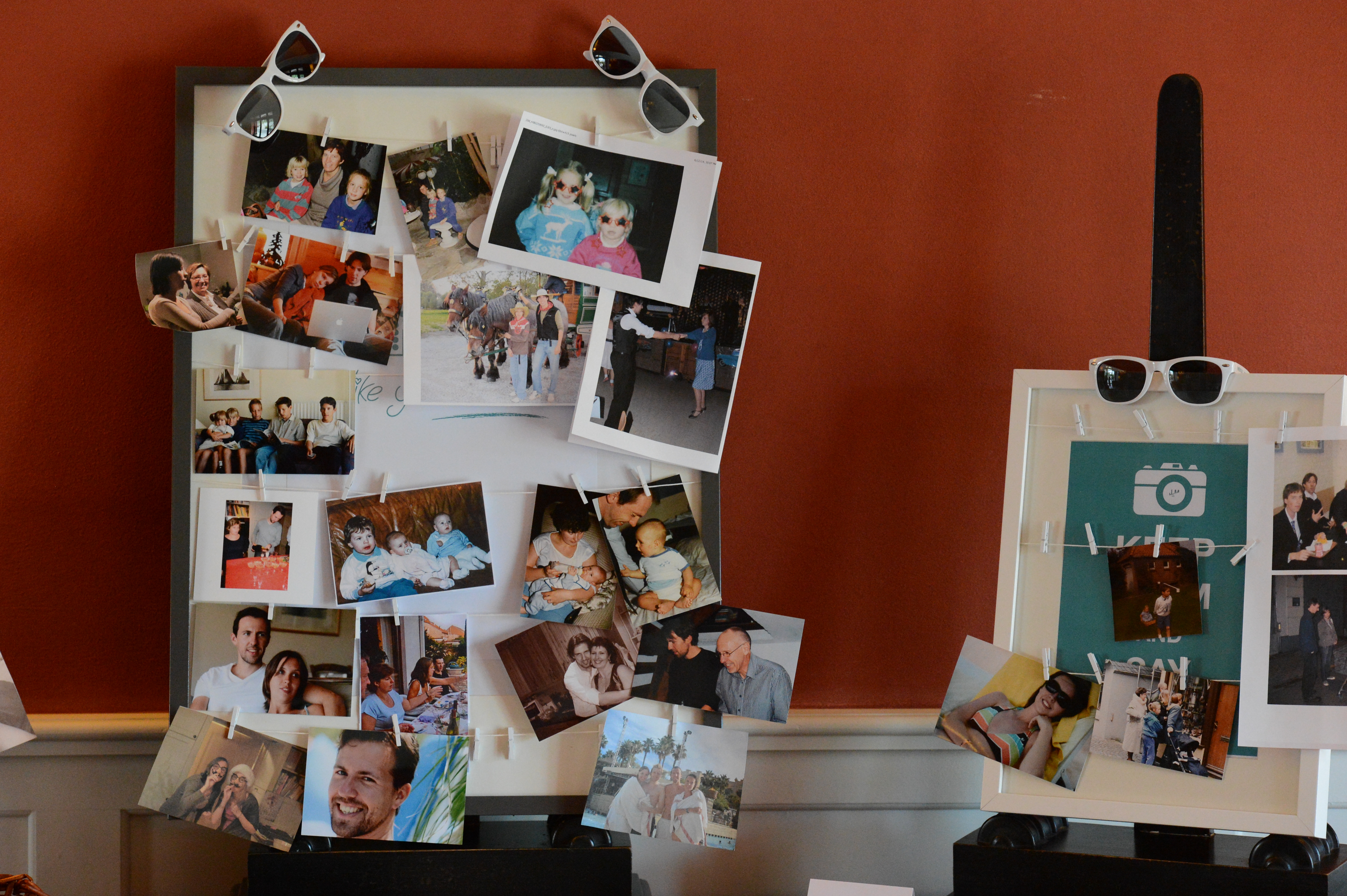 A wedding display with framed boards holding family and childhood photos, clipped with small pins and decorated with sunglasses.