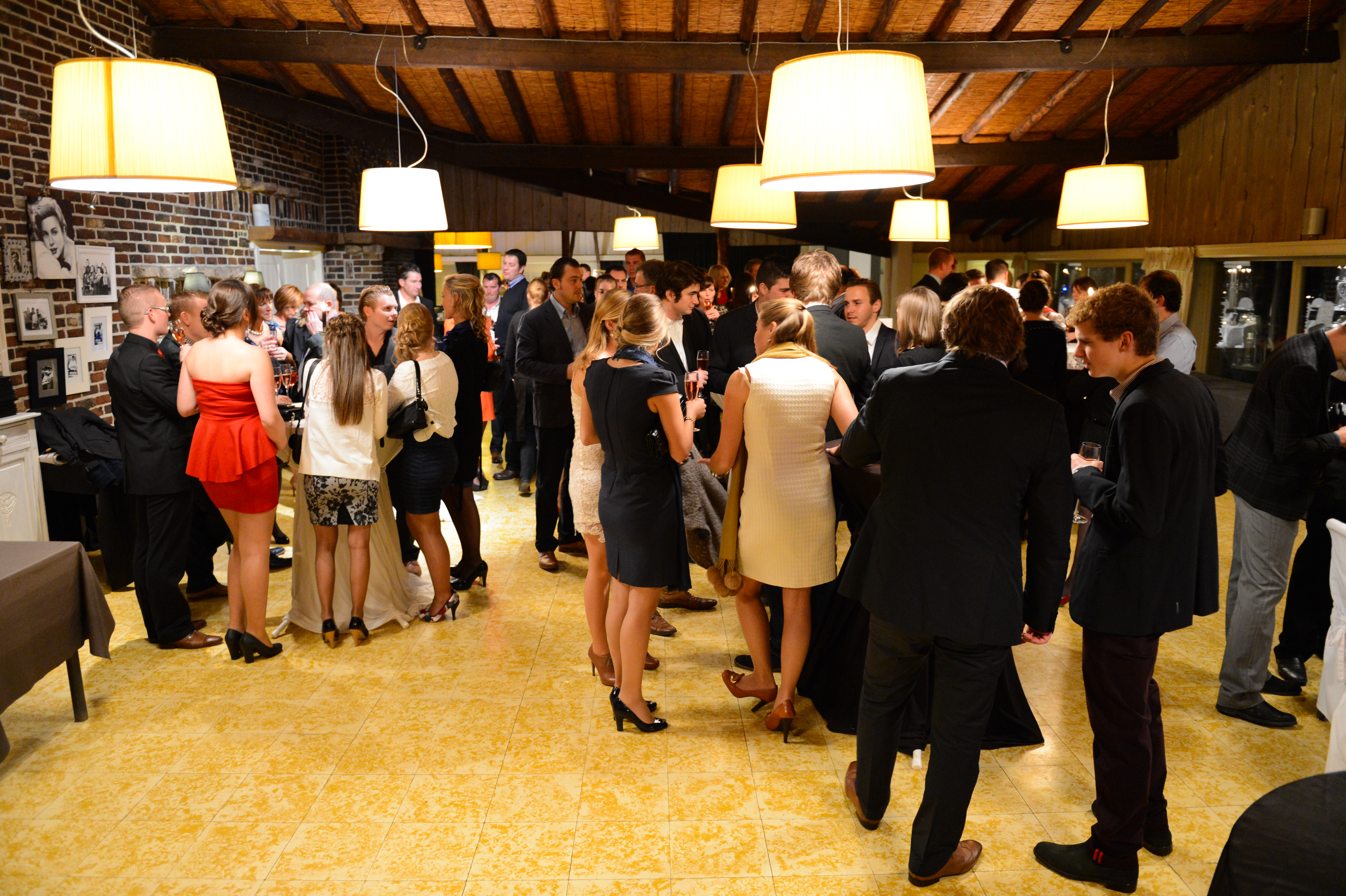Guests in formal attire gather indoors, chatting and holding drinks at a wedding reception.