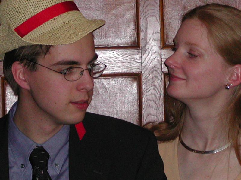 A man in a suit and straw hat looks away while a woman beside him smiles at him.