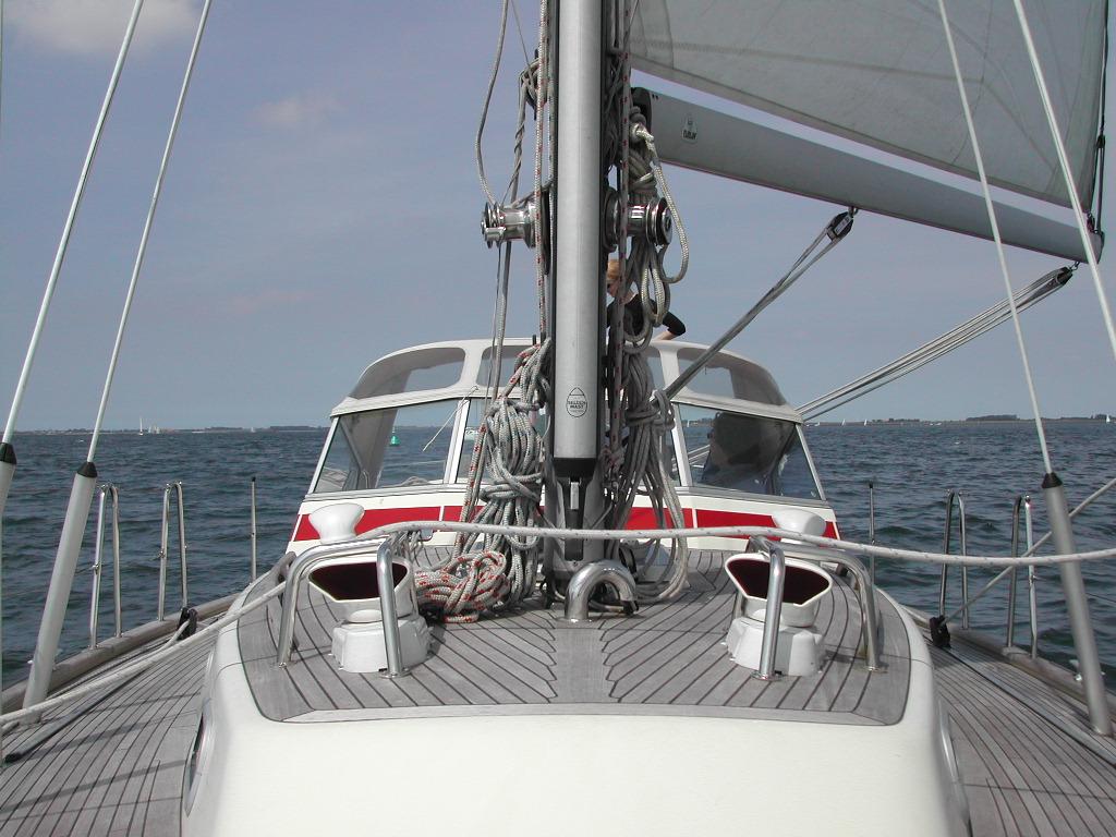 View from the deck of a sailing boat on the water, with sails up and ropes secured to the mast.