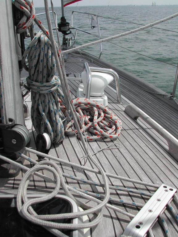 Coiled and bundled ropes on the wooden deck of a sailboat, with the ocean visible in the background.