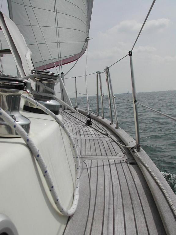 View from the deck of a sailing boat with ropes and winches, moving through the water under a raised sail.
